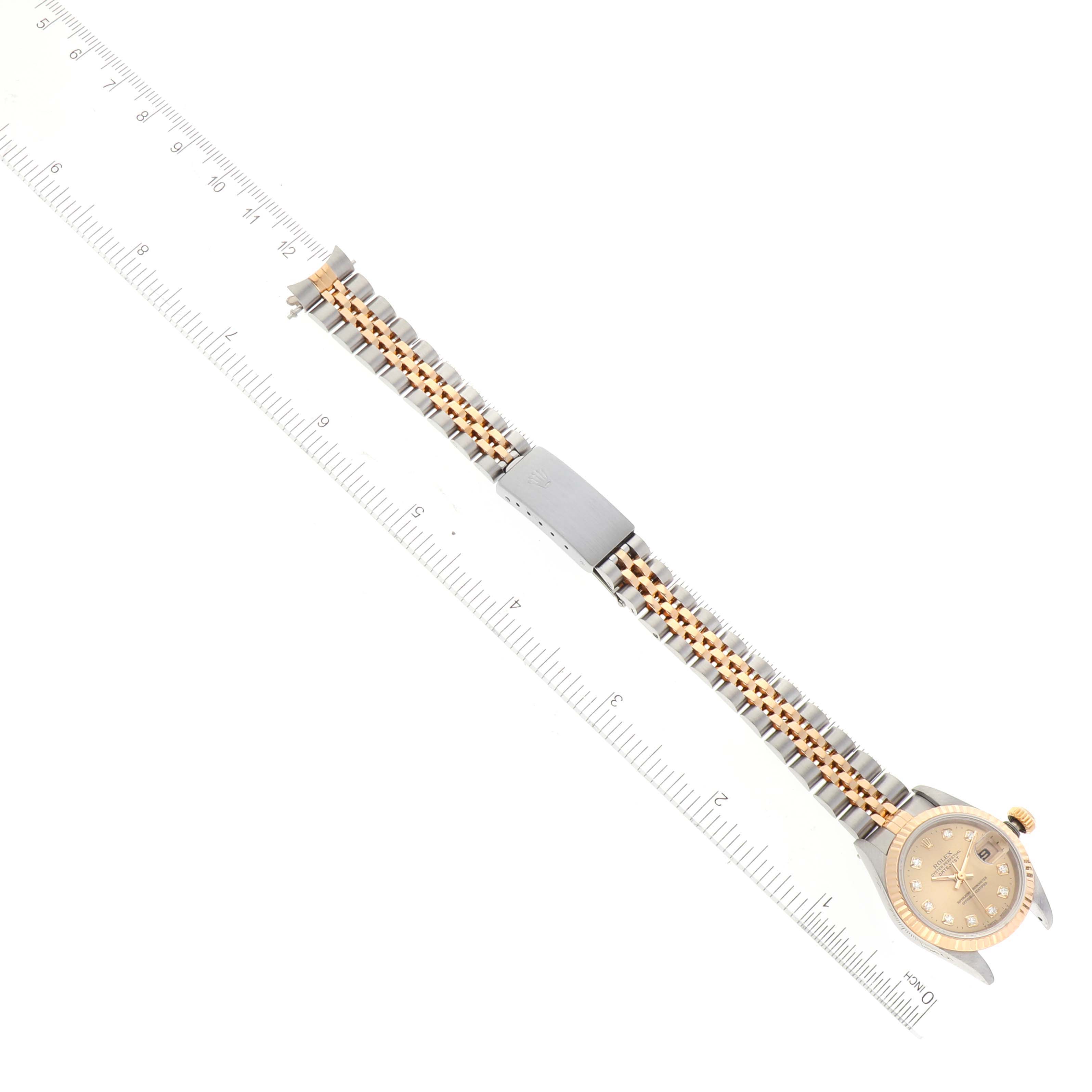 The image shows a Rolex Datejust 69173 Women
s Steel and Gold (two tone) Champagne Dial 69173 Women
s Steel and Gold (two tone) Champagne Dial watch laid flat next to a ruler, highlighting the bracelet, dial, and clasp from a top-down angle.