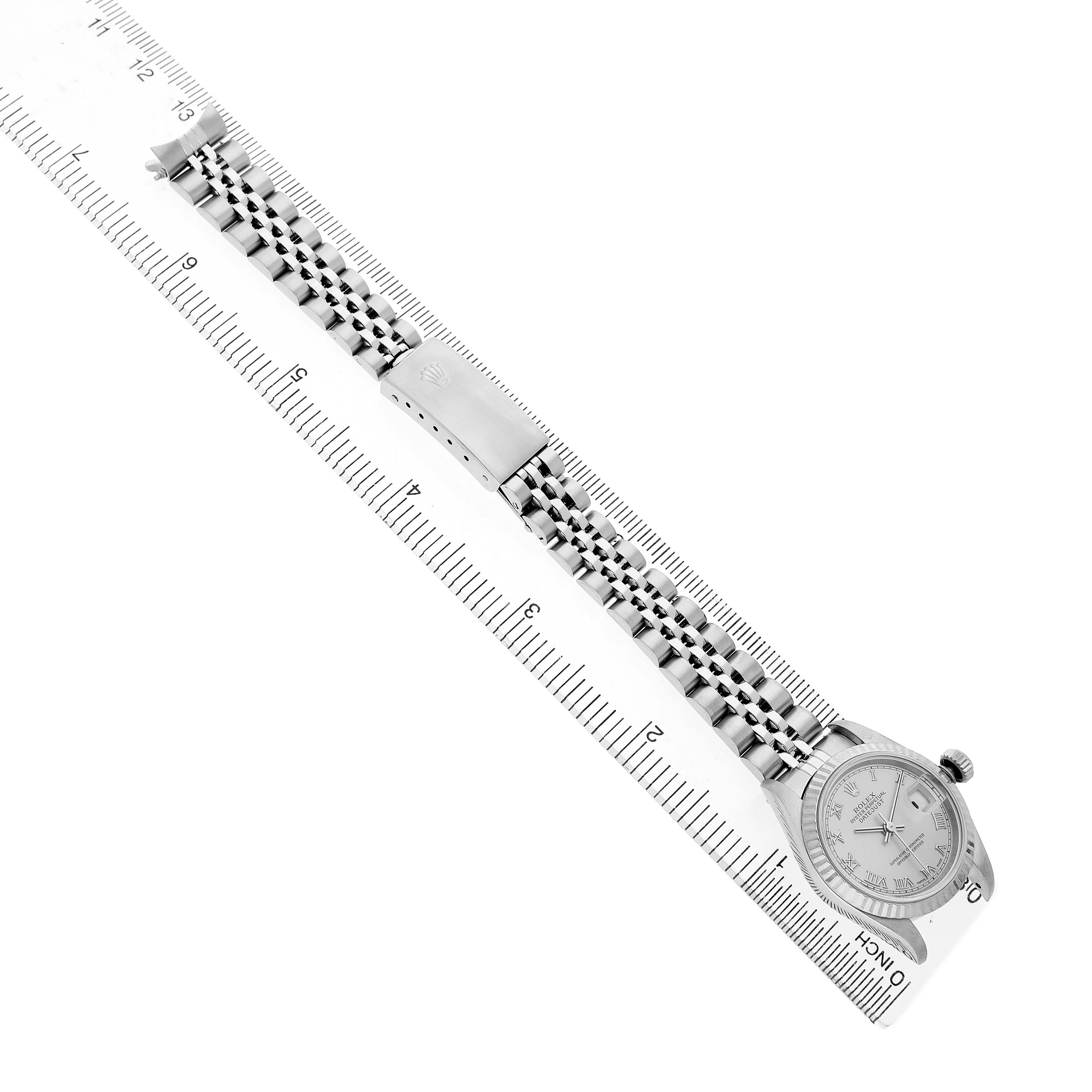 The Rolex Datejust 79174 Women's Stainless Steel Silver Dial watch is shown at a top-down angle, displaying the face, bezel, bracelet, and clasp placed alongside a ruler.