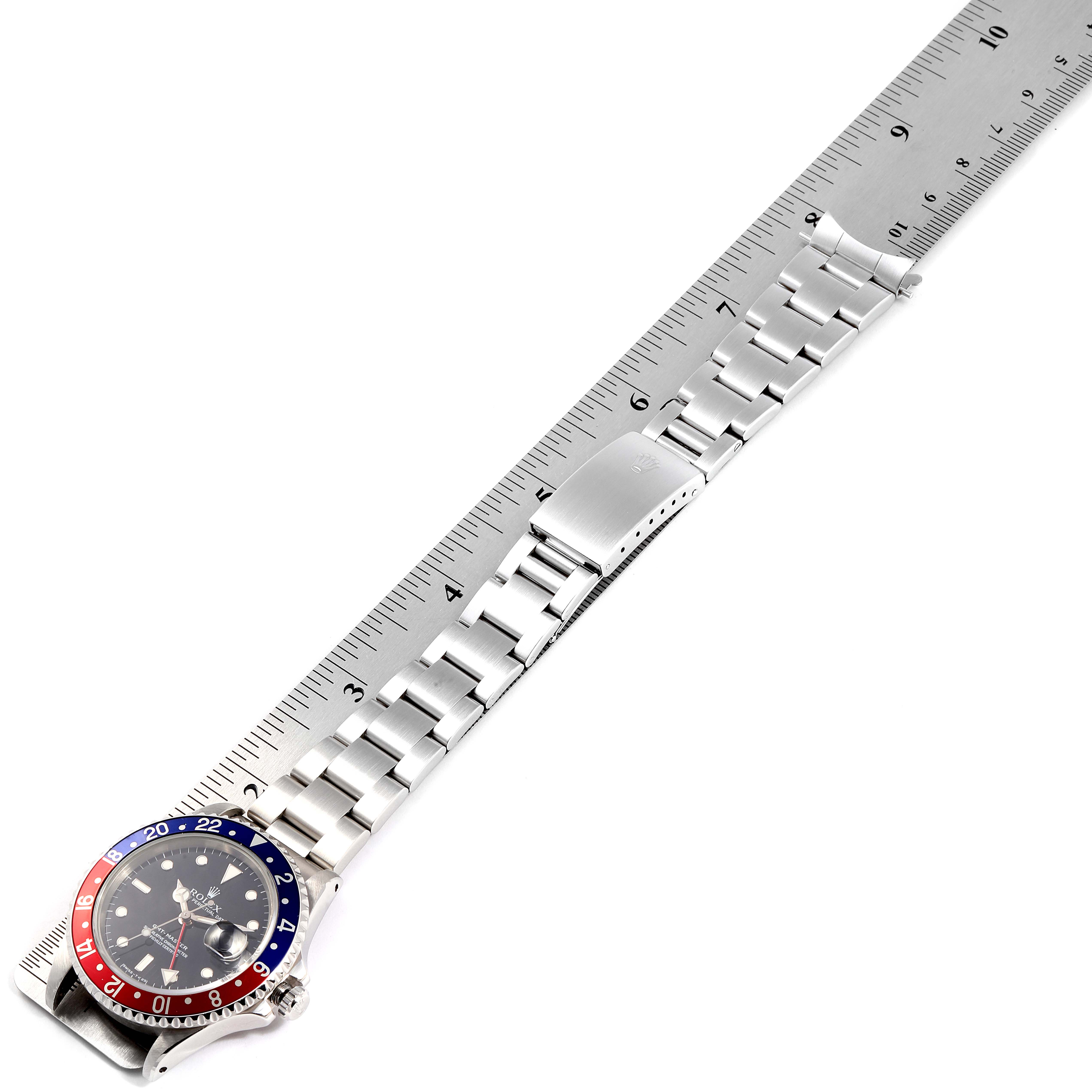 This image shows the Rolex GMT-Master 16700 Men's Stainless Steel Black Dial 16700 Men's Stainless Steel Black Dial watch laying flat next to a ruler, highlighting its bezel, dial, and bracelet.