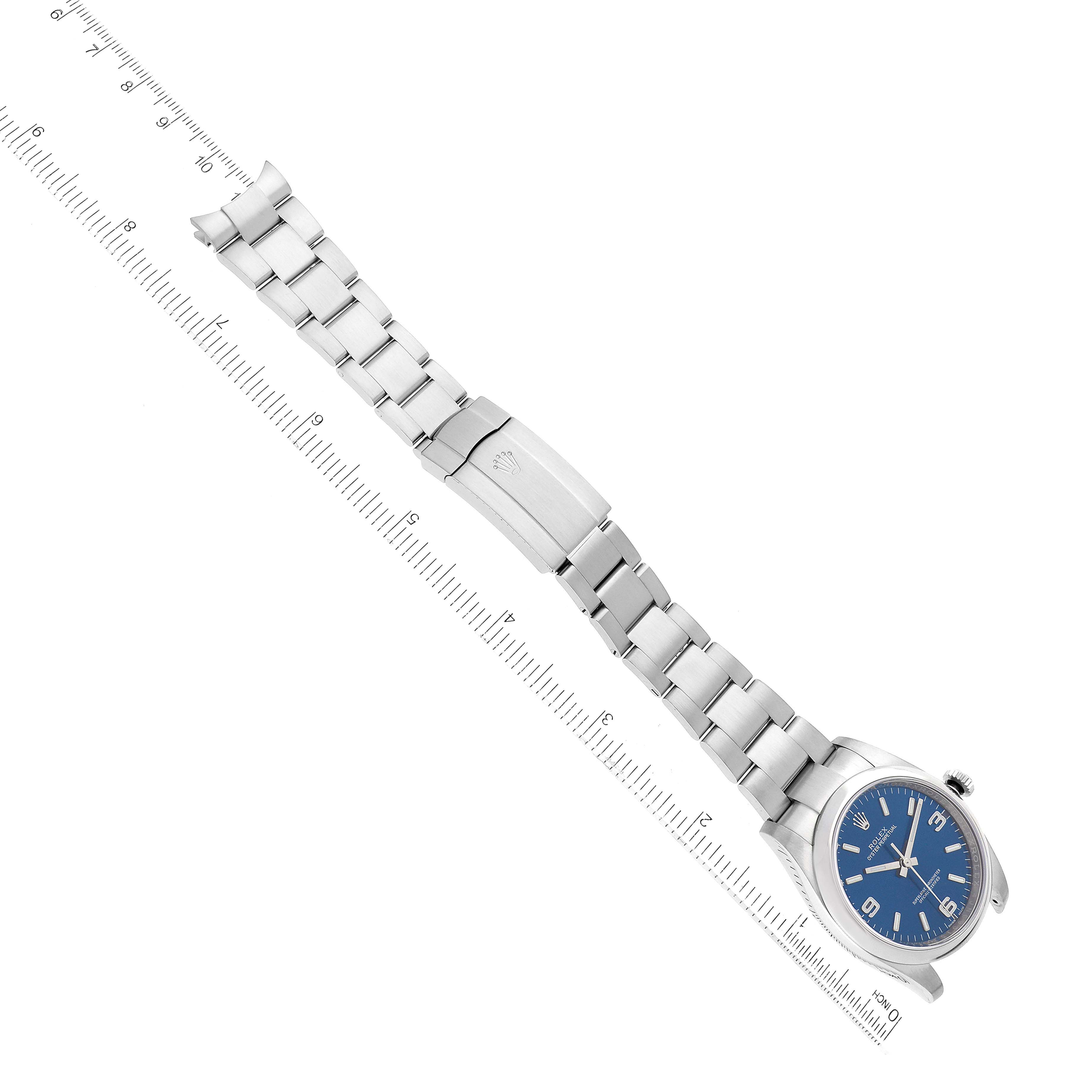 The image shows a Rolex Oyster Perpetual 116000 Men
s Stainless Steel Blue Dial 116000 Men
s Stainless Steel Blue Dial watch lying flat with its metal bracelet fully extended alongside a ruler for scale.