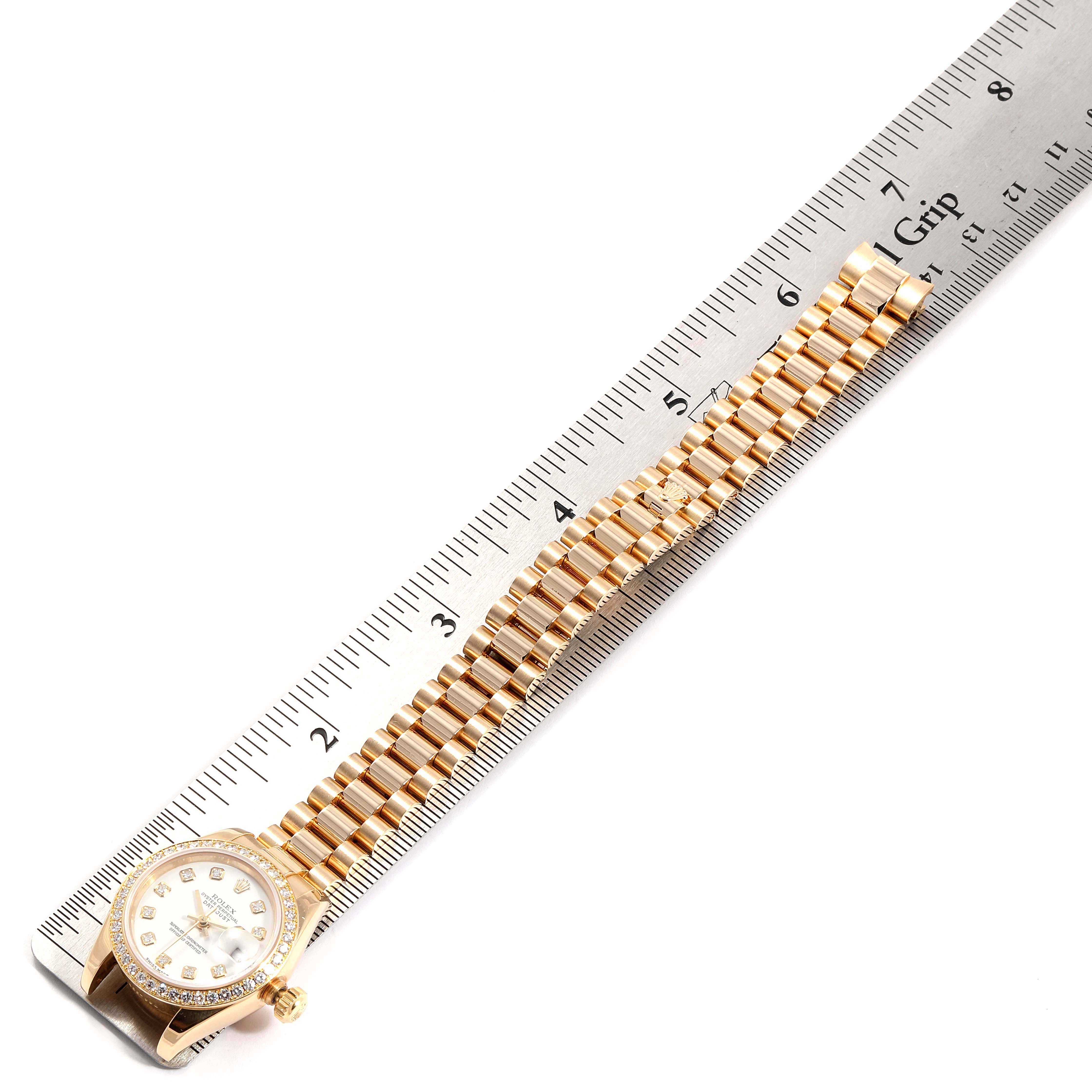 The Rolex President 179138 Women
s Yellow Gold White Dial 179138 Women
s Yellow Gold White Dial watch is shown from above, with its gold bracelet laid out next to a ruler for measurement.