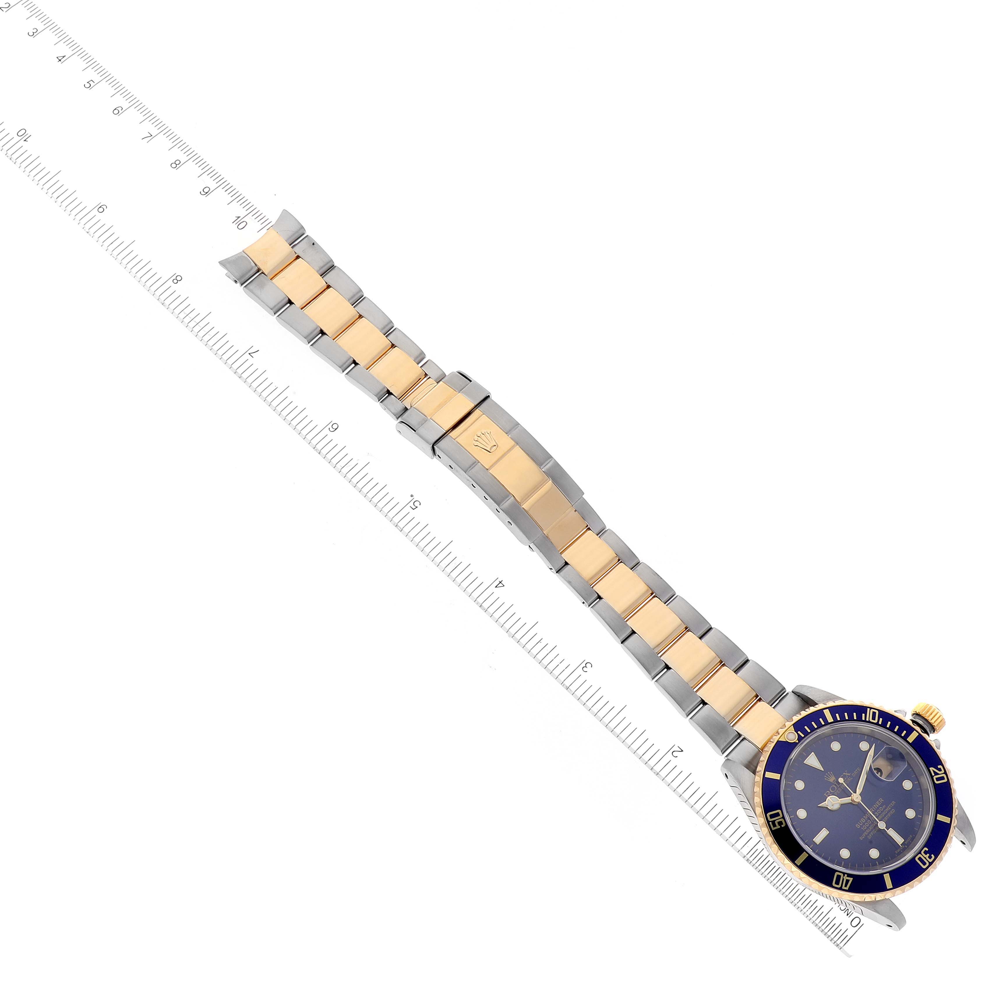 The image shows a top-down view of the Rolex Submariner 16613 Men's Steel and Gold (two tone) Blue Dial 16613 Men's Steel and Gold (two tone) Blue Dial watch, displaying its bracelet, clasp, and face along with a ruler for scale.