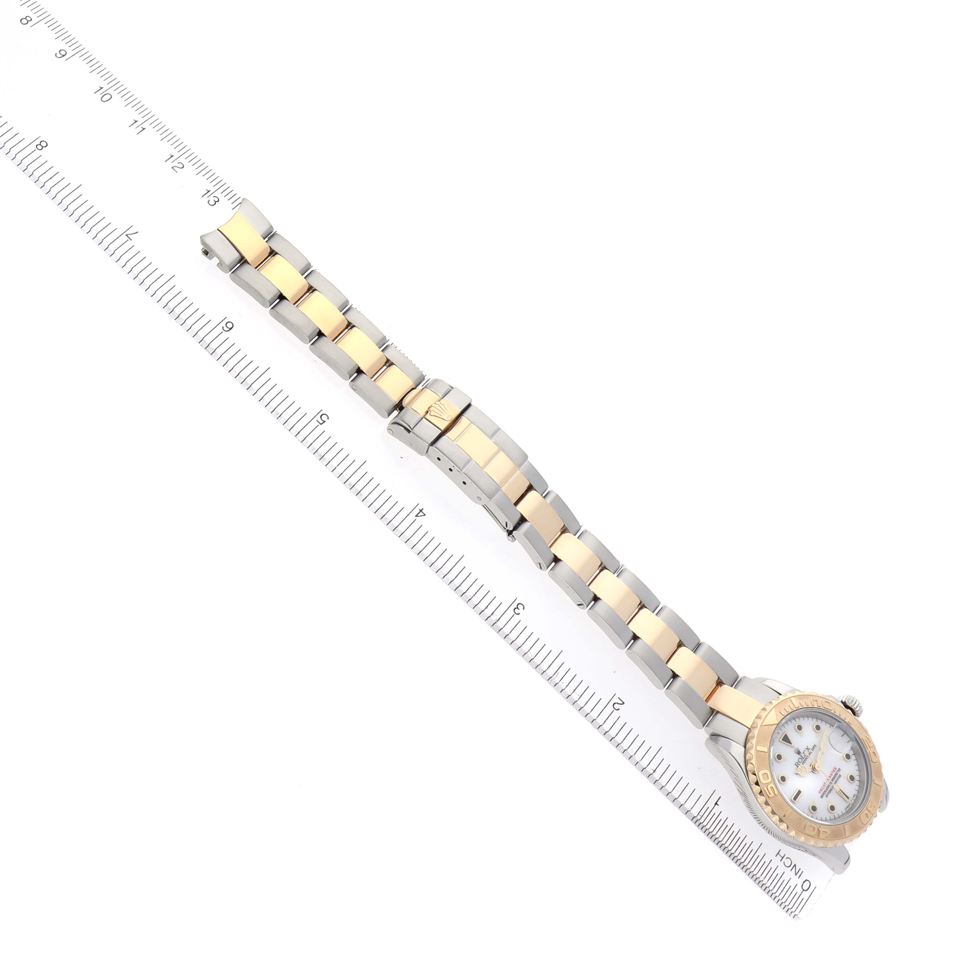 The image shows a top view of a Rolex Yacht-Master 69623 Women
s Steel and Gold (two tone) White Dial 69623 Women
s Steel and Gold (two tone) White Dial watch with a two-tone bracelet next to a ruler.