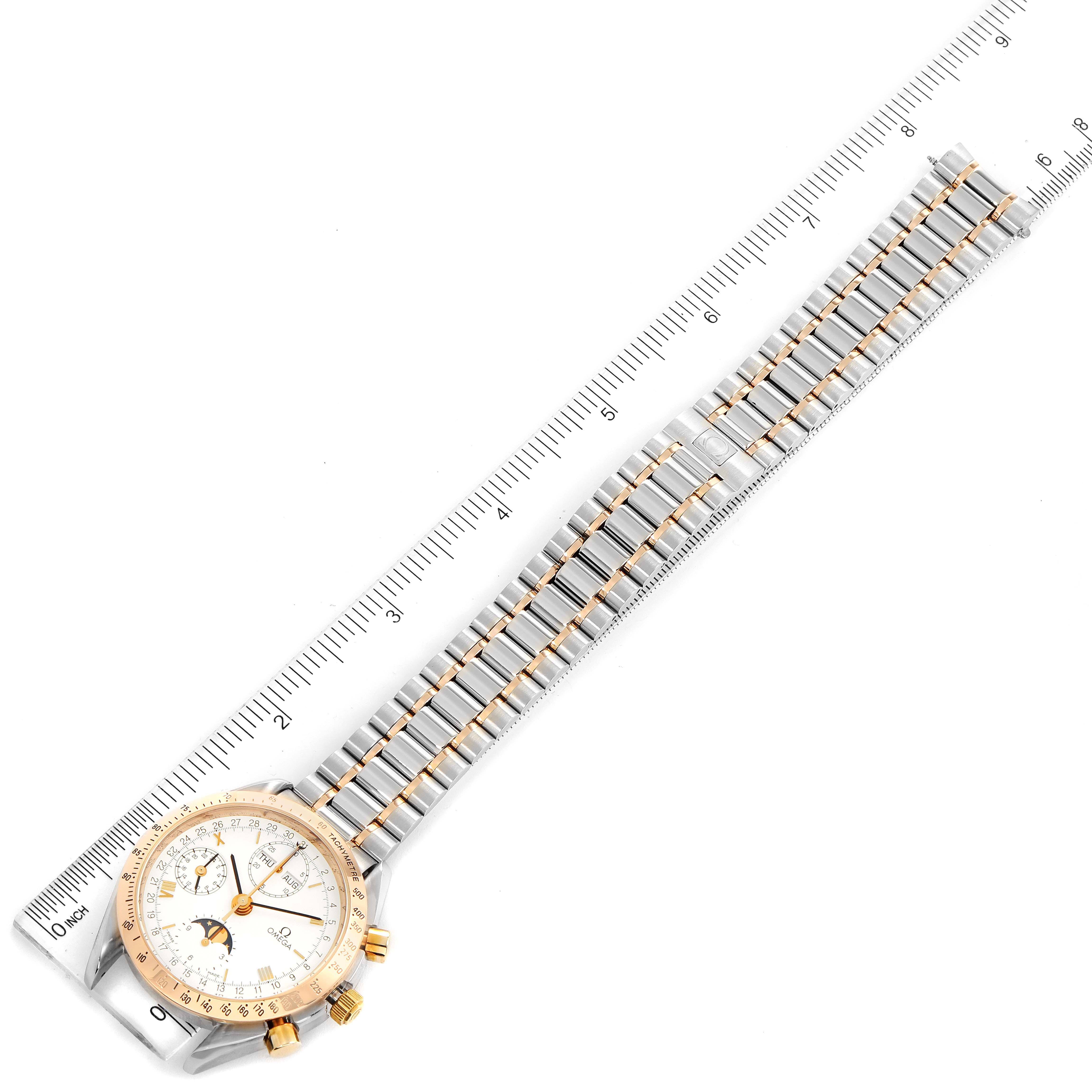 The Omega Speedmaster 3330.20.00 Men's Steel and Gold (two tone) White Dial 3330.20.00 Men's Steel and Gold (two tone) White Dial watch with a stainless steel and gold bracelet is shown from a top-down angle with a ruler beside it.