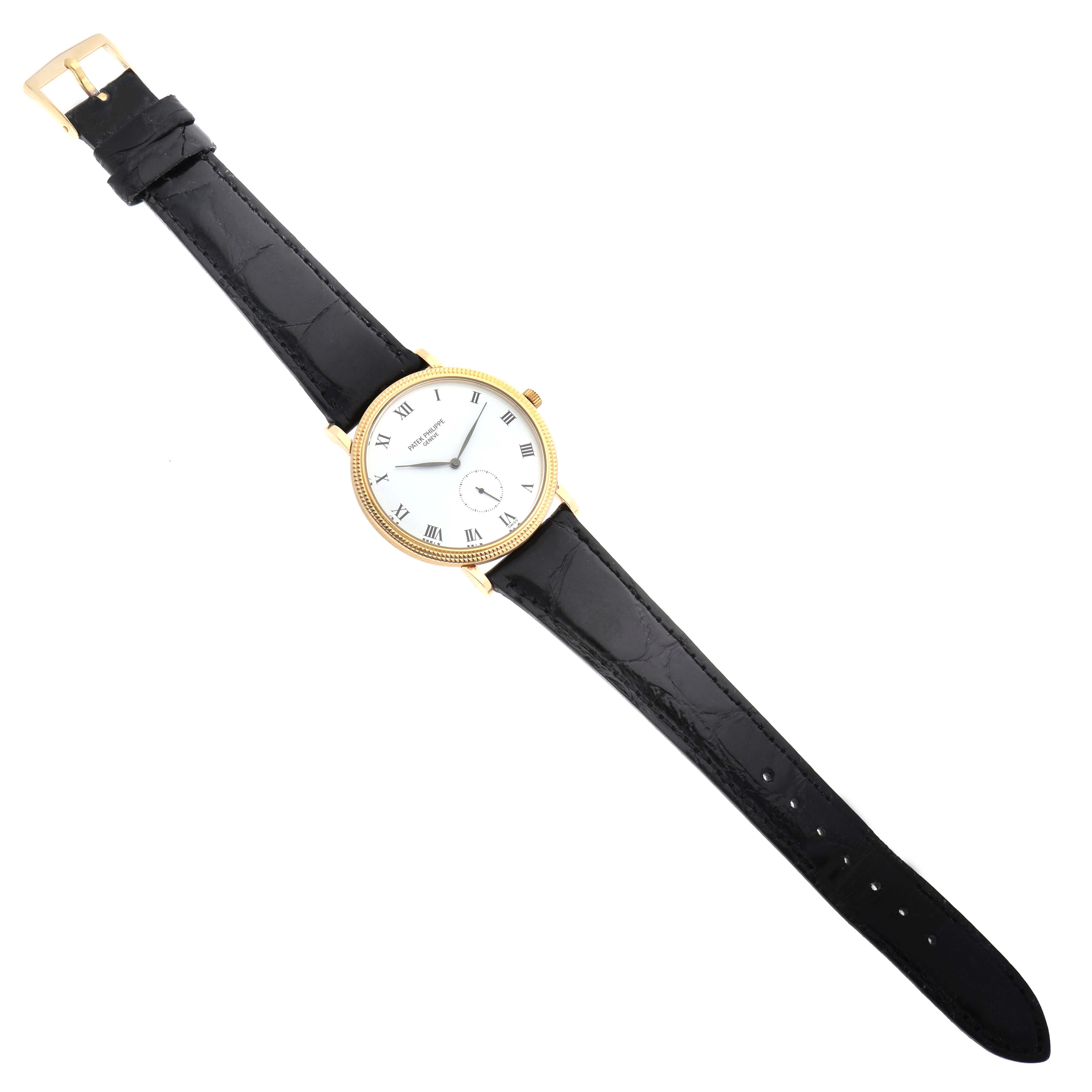The image shows a top-down view of a Patek Philippe Calatrava 3919J Men's Yellow Gold White Dial 3919J Men's Yellow Gold White Dial watch with a gold case, white dial, and black leather strap.