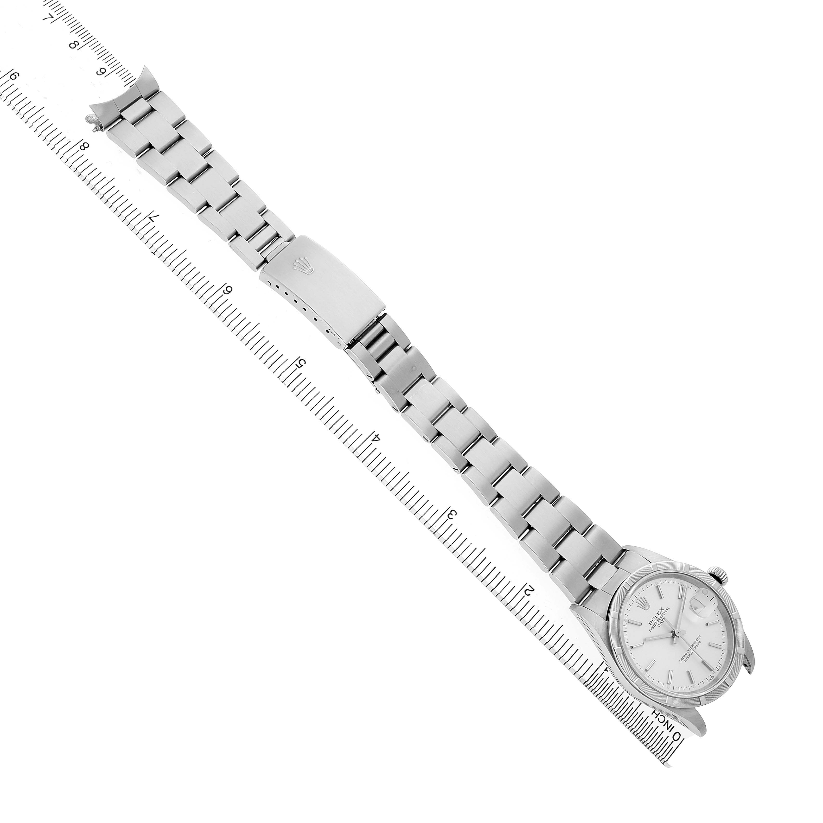 The Rolex Date 15210 Men's Stainless Steel Silver Dial watch is shown at an angled top view, displaying the face, bracelet, and clasp beside a ruler.