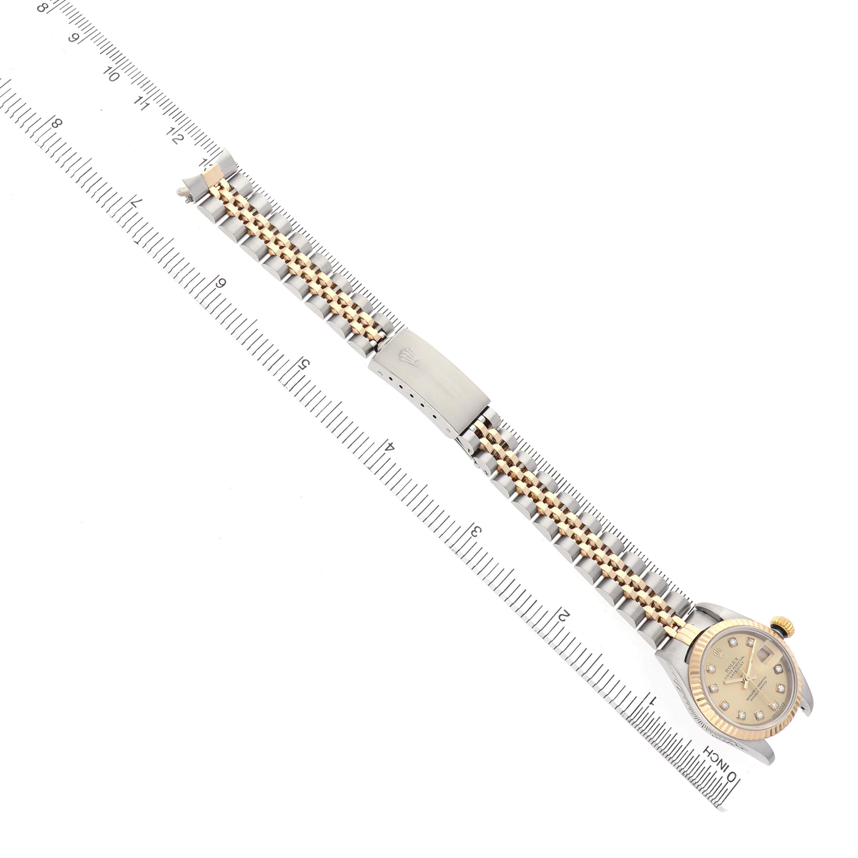The Rolex Datejust 79173 Women's Steel and Gold (two tone) Champagne Dial watch is shown from a top-down angle, featuring the full bracelet, clasp, and watch face alongside a ruler.