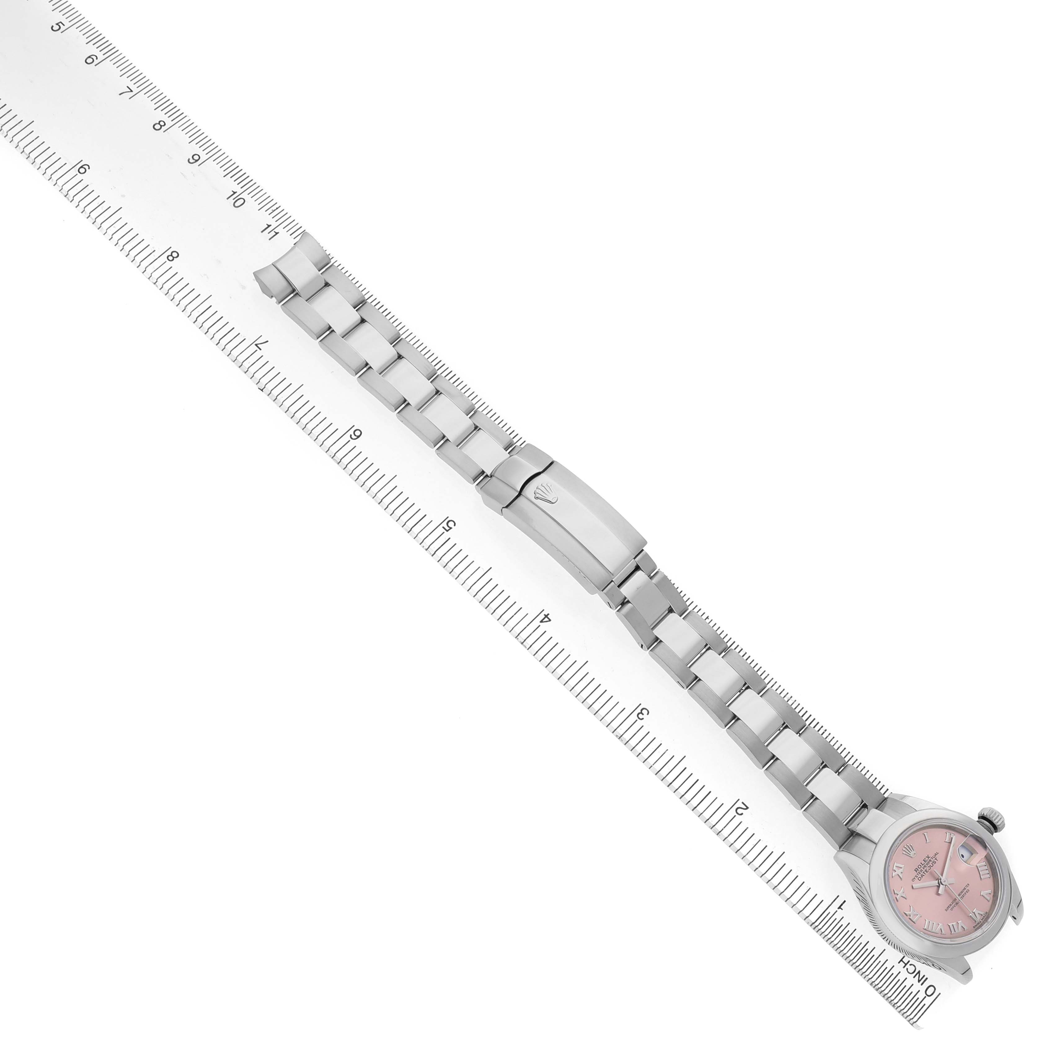 The image shows a Rolex Datejust 279160 Women's Stainless Steel Pink Dial watch at a diagonal angle, highlighting the pink dial, bezel, bracelet, and clasp next to a ruler.