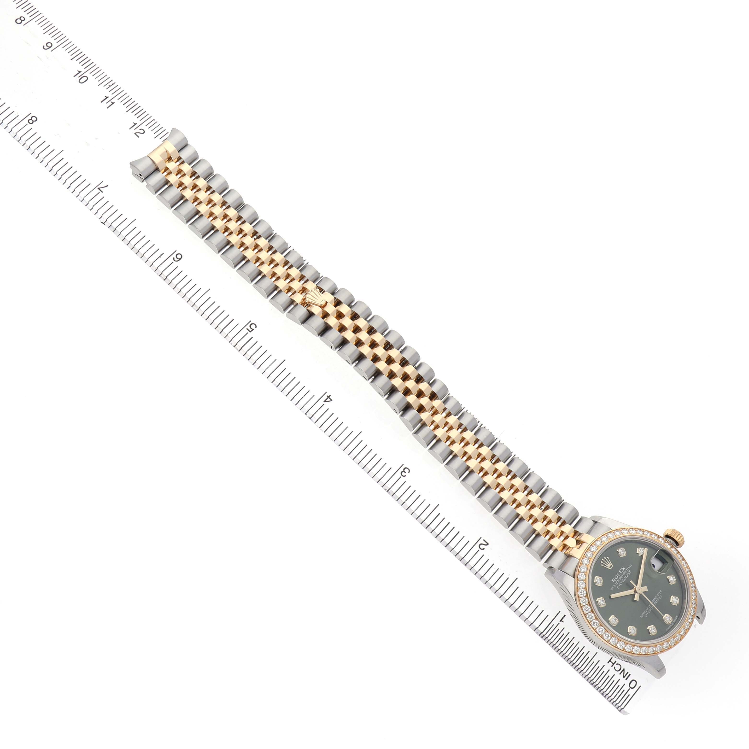 The Rolex Datejust 278383 Women's Steel and Gold (two tone) Green Dial watch is shown from an overhead view, displaying the bracelet and the watch face alongside a ruler.