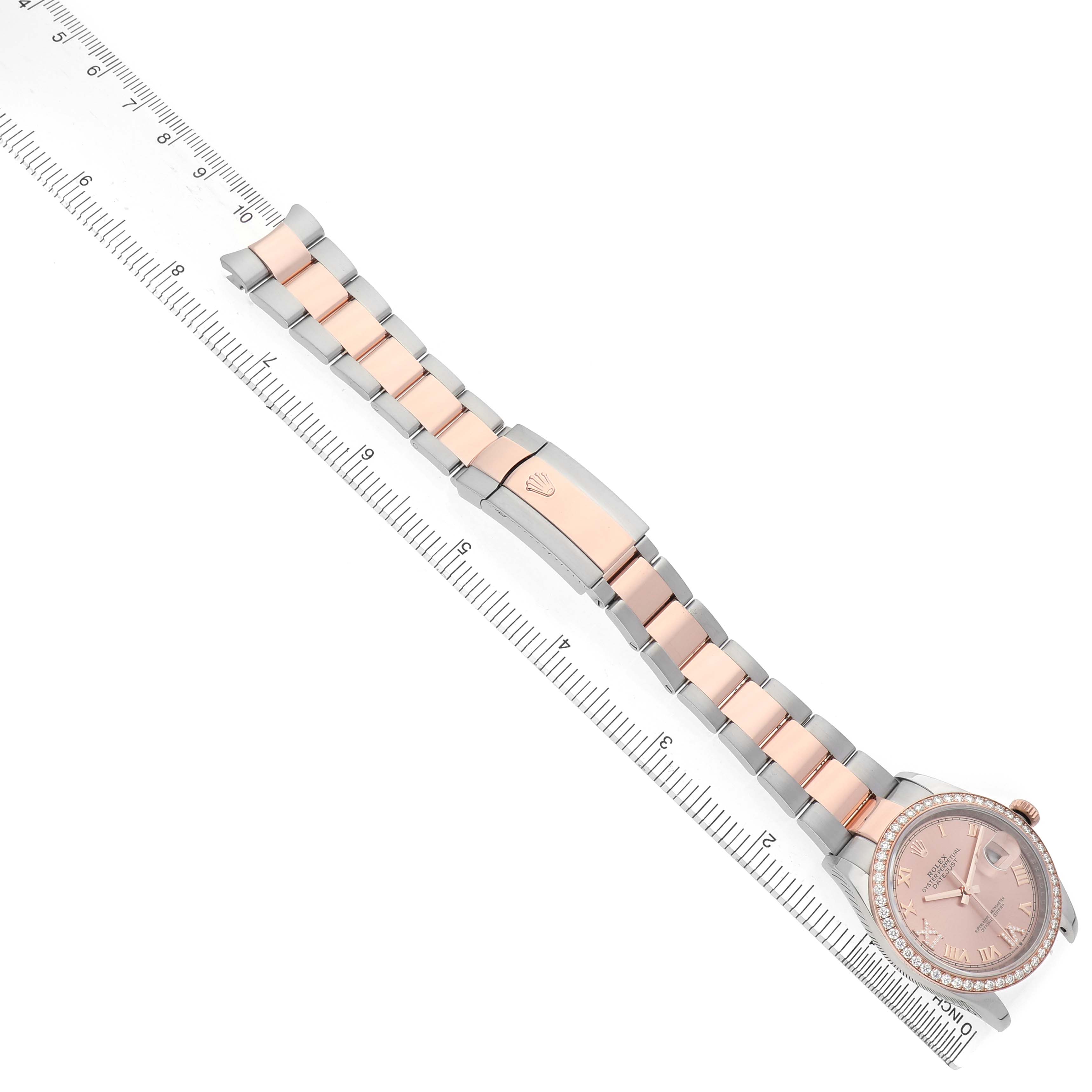 The Rolex Datejust 126281 Men's Steel and Gold (two tone) Pink Dial watch is shown at a top-down angle, displaying its face, bracelet, and clasp against a ruler for scale.