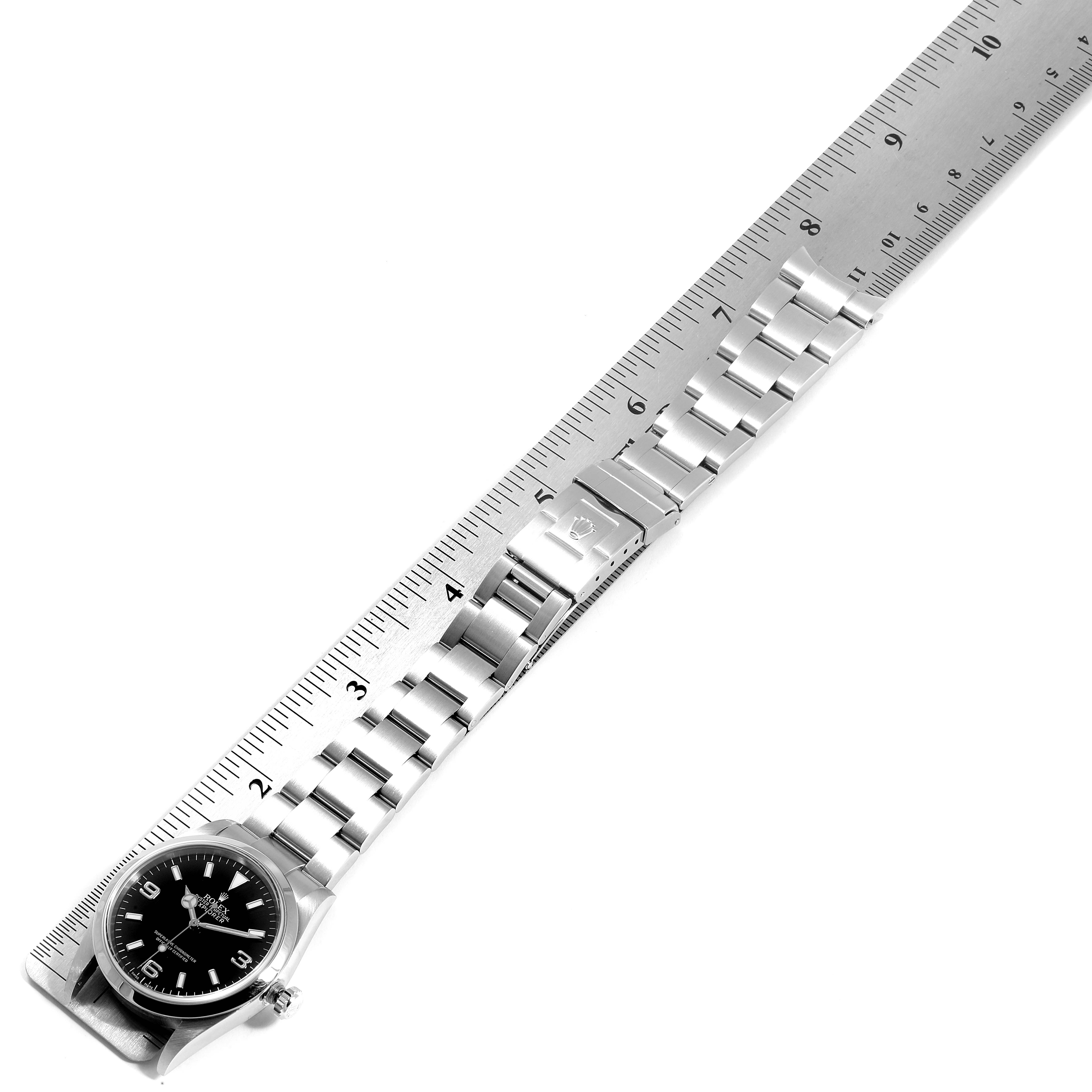A Rolex Explorer 114270 Men
s Stainless Steel Black Dial 114270 Men
s Stainless Steel Black Dial watch is shown from an overhead angle alongside a ruler, showcasing its face, bracelet, and clasp.