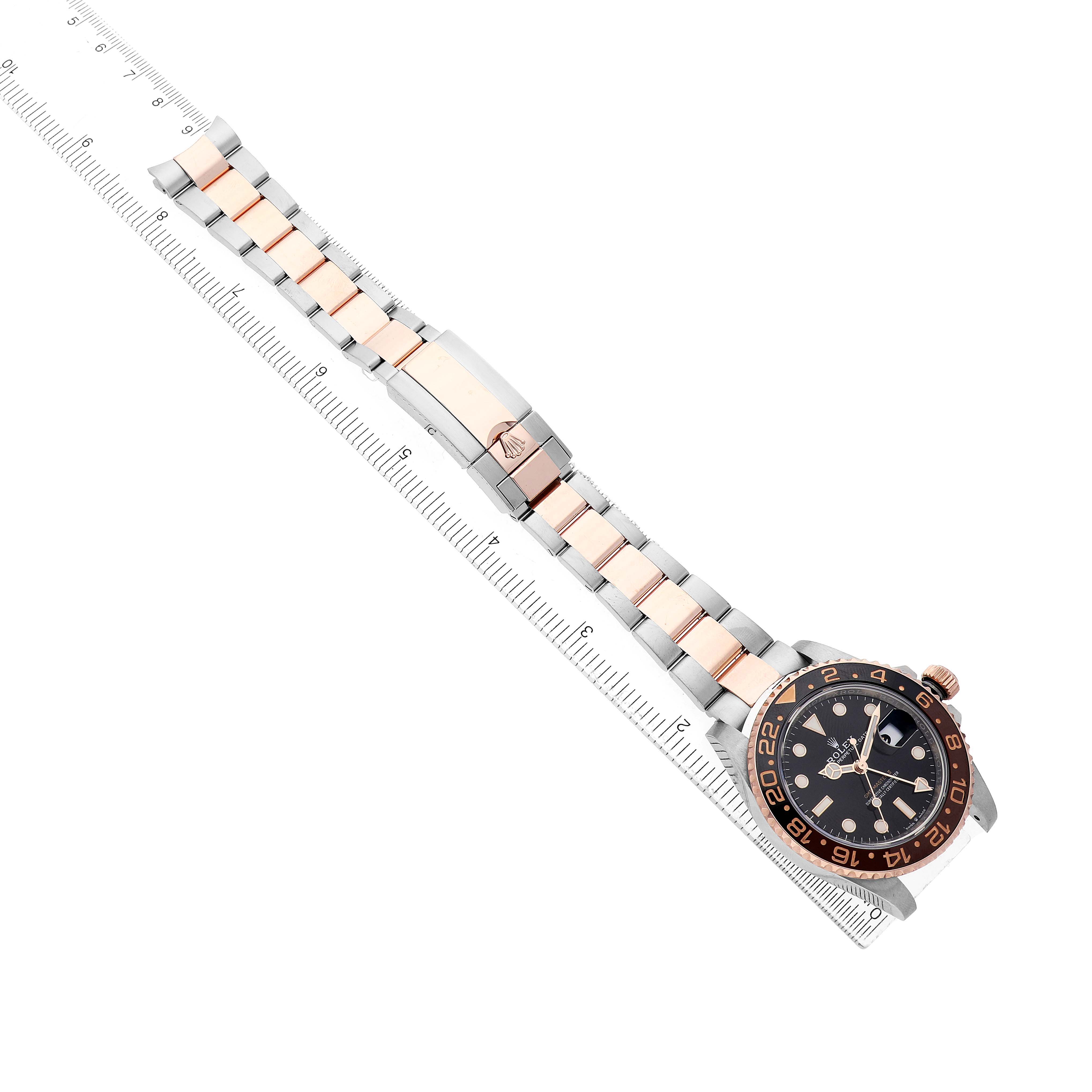 The Rolex GMT-Master 126711 Men's Steel and Gold (two tone) Black Dial watch is shown at an angle displaying its face, bezel, and full bracelet alongside a ruler.