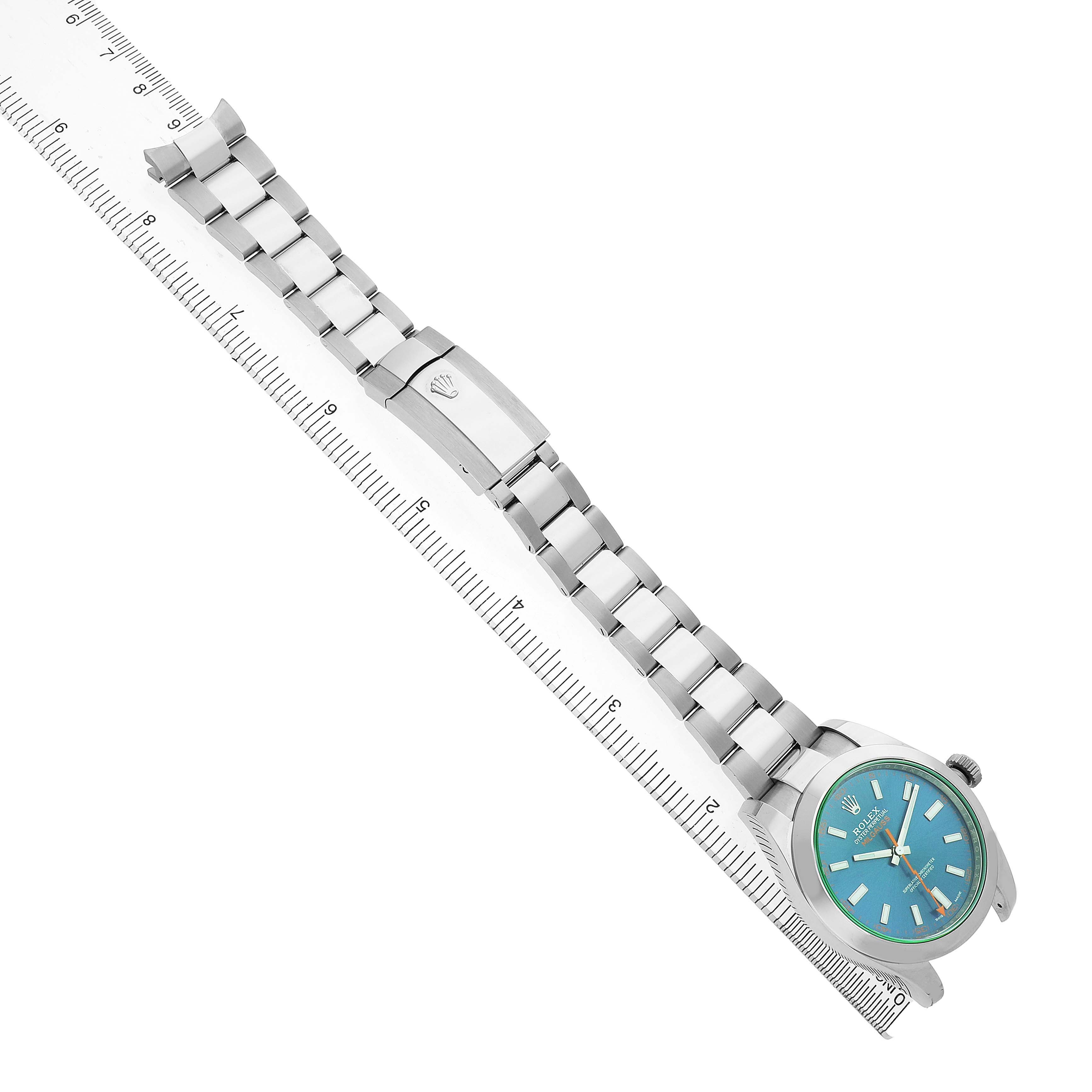 The Rolex Milgauss 116400GV Men's Stainless Steel Blue Dial watch is shown from an angled top view, highlighting the face, bezel, bracelet, and clasp alongside a ruler.