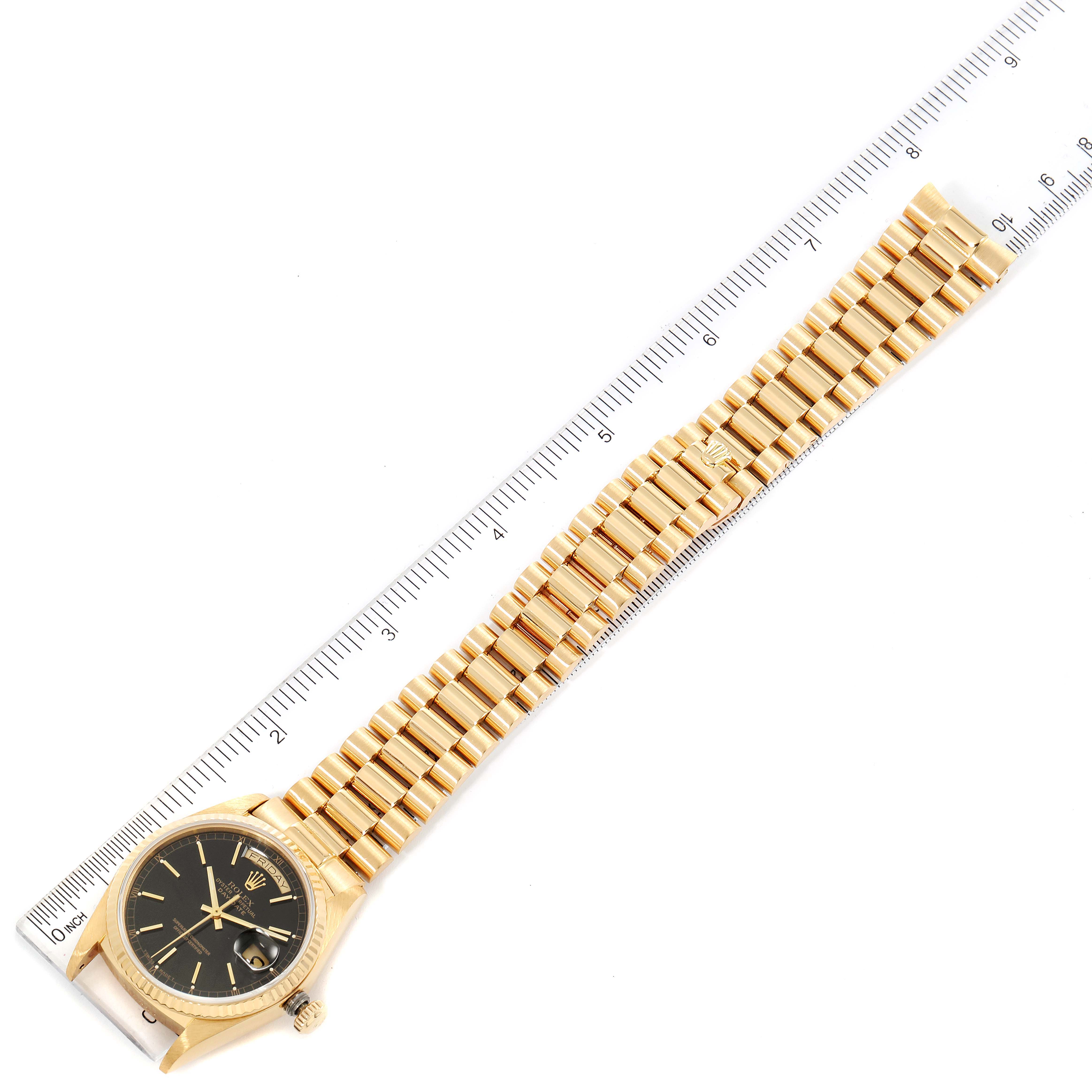 This image shows a Rolex President 18038 Men's Yellow Gold Black Dial 18038 Men's Yellow Gold Black Dial model watch face-up with its bracelet laid out next to a ruler for measurement.