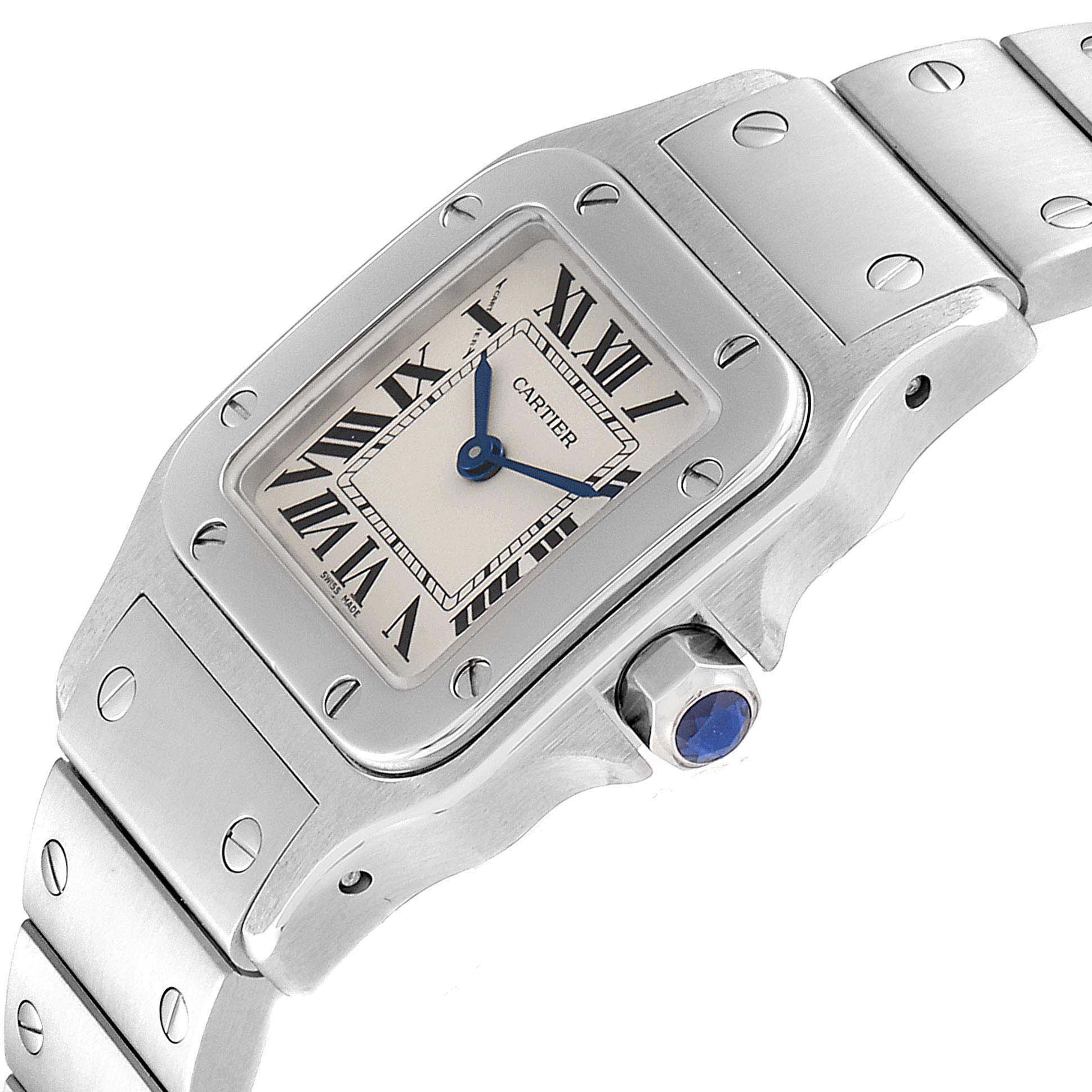 The image shows a close-up angle of the Santos model by Cartier, highlighting the face, bezel, crown with blue gem, and part of the bracelet.