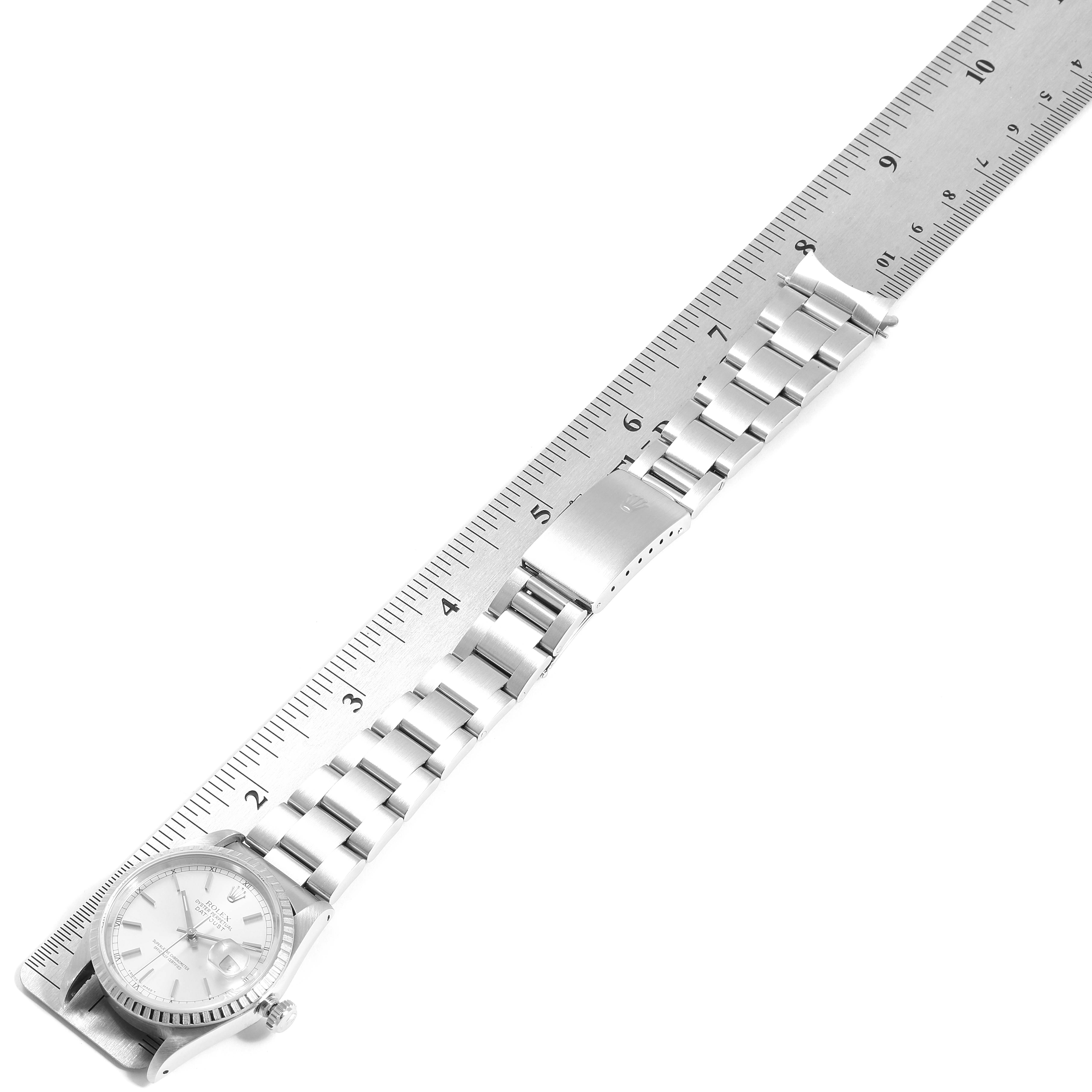 This Rolex Datejust 16220 Men's Stainless Steel Silver Dial 16220 Men's Stainless Steel Silver Dial watch is shown from the top angle, with its bracelet and clasp extending alongside a ruler.