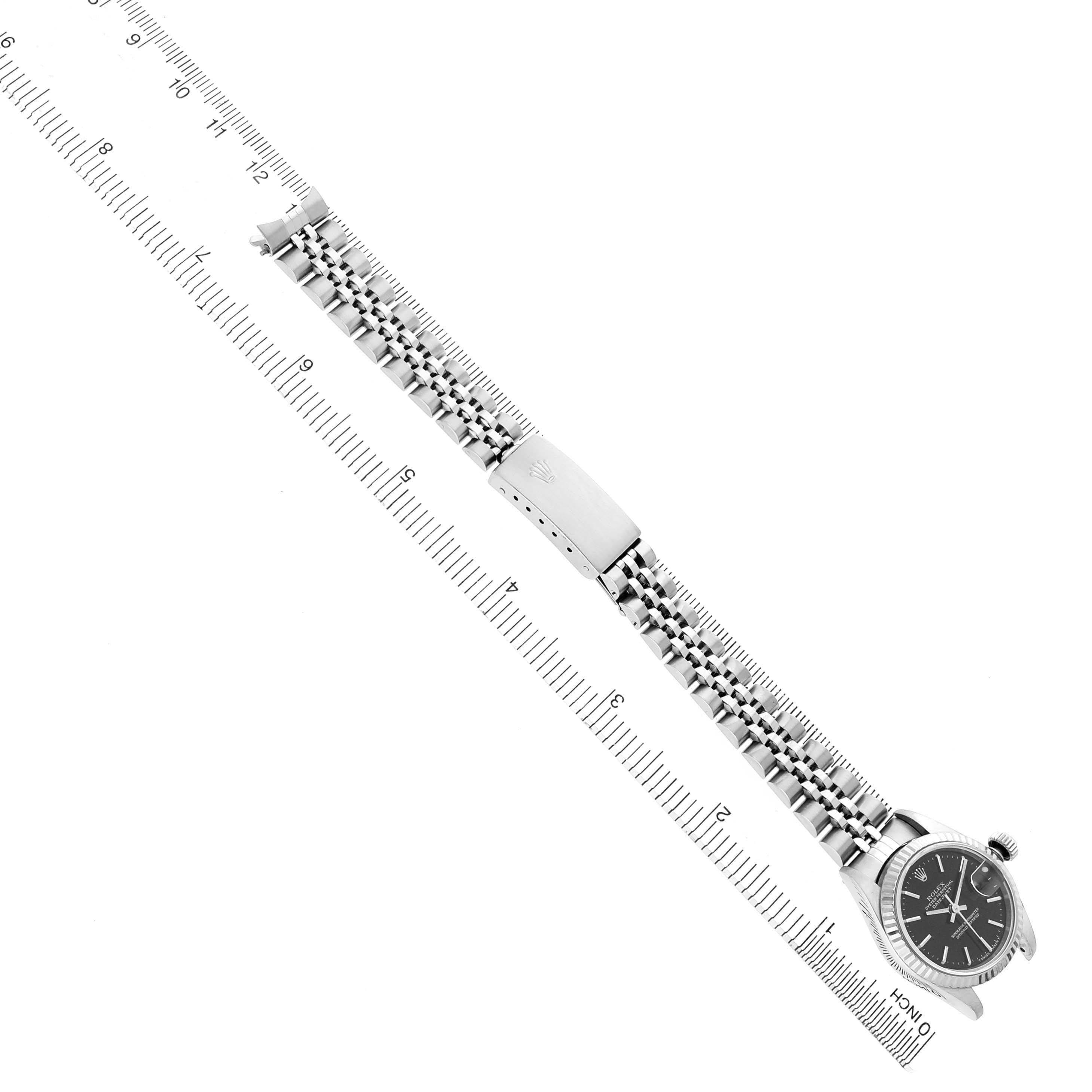 The image shows a Rolex Datejust 69174 Women's Stainless Steel Black Dial watch laid flat, displaying the face, crown, jubilee bracelet, and clasp alongside a measuring ruler.