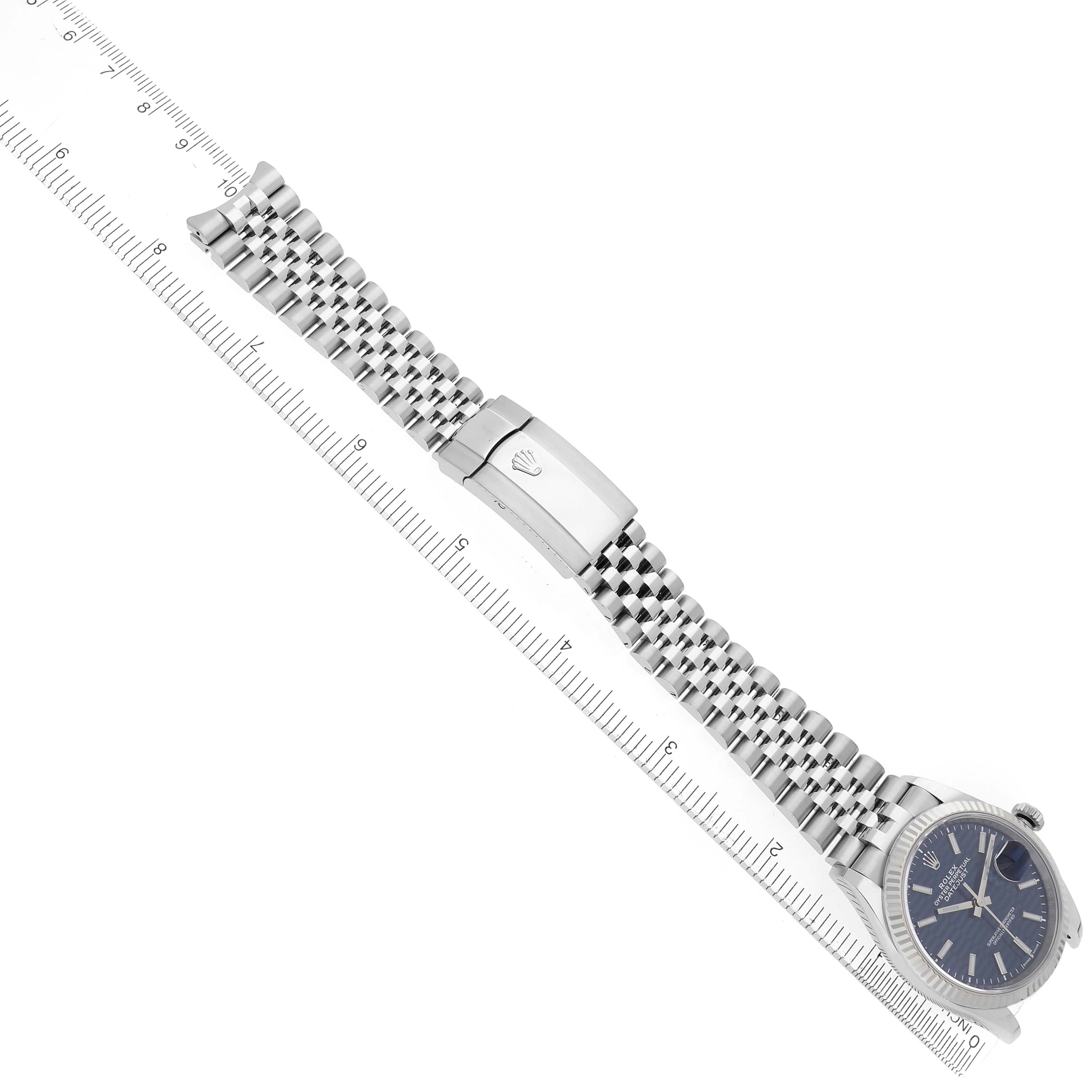 The Rolex Datejust 126234 Men
s Stainless Steel Blue Dial 126234 Men
s Stainless Steel Blue Dial watch is shown from above, featuring its bracelet and clasp, with a ruler for scale.