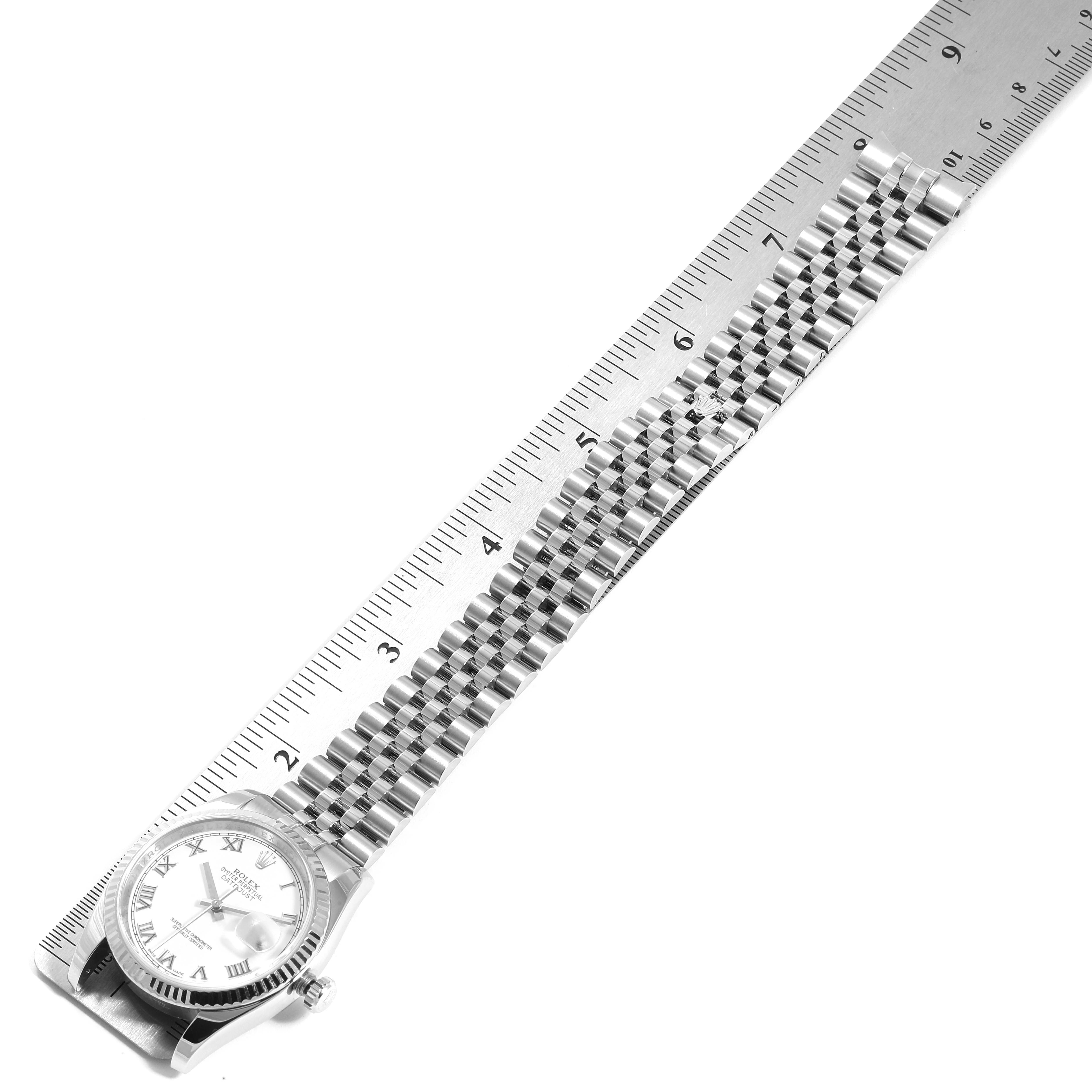 The Rolex Datejust 116234 Men's Stainless Steel White Dial 116234 Men's Stainless Steel White Dial watch is shown from a top-down angle, displaying the watch case, dial, crown, and bracelet alongside a ruler.