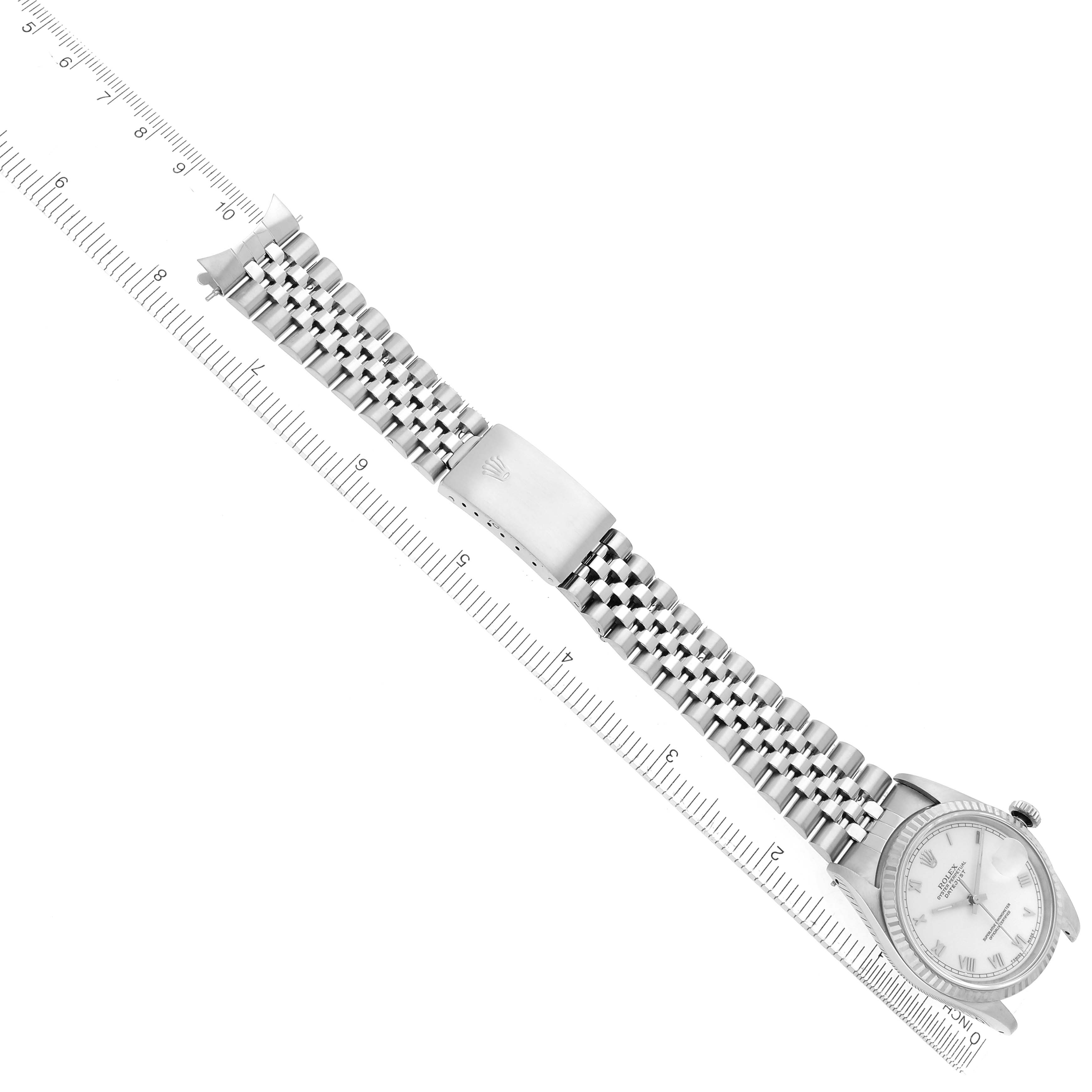 The Rolex Datejust 16234 Men
s Stainless Steel White Dial 16234 Men
s Stainless Steel White Dial watch is shown from above, displaying the bracelet, clasp, and part of the watch face next to a ruler.