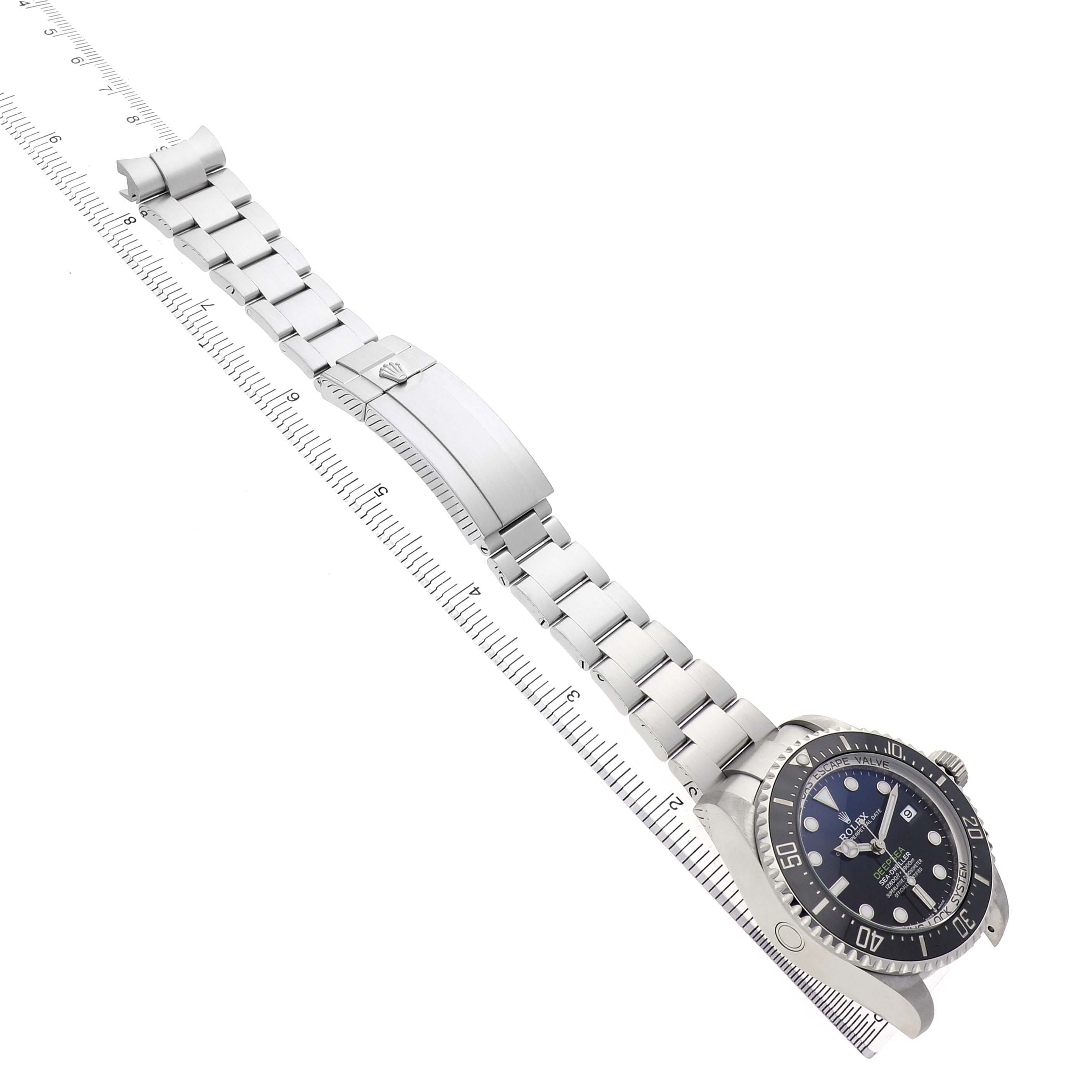 The Rolex Sea-Dweller 136660 Men's Stainless Steel Blue Dial watch is shown at an angle, featuring the face, bezel, and bracelet, with a ruler alongside for scale.