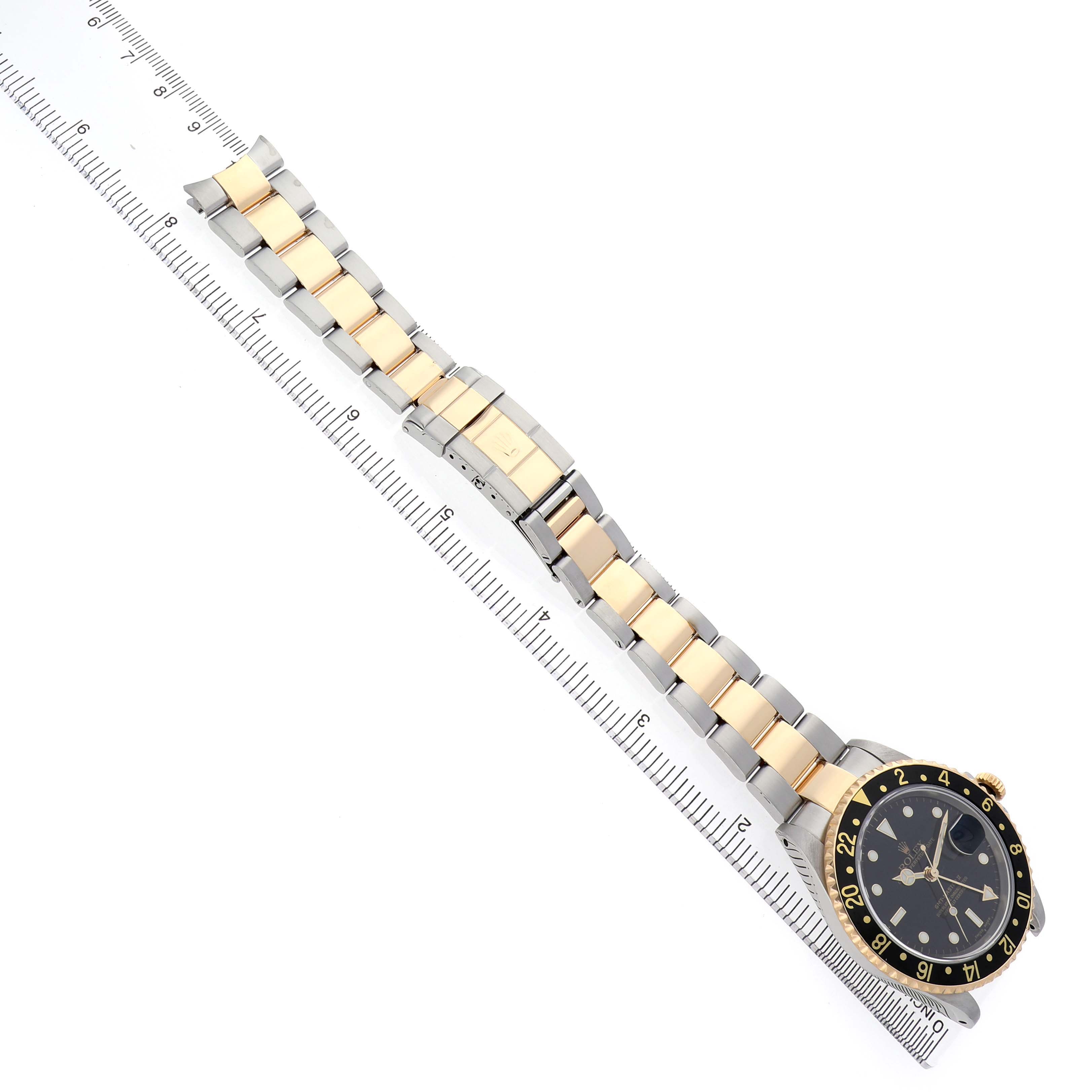The Rolex GMT-Master 16713 Men's Stainless Steel Black Dial watch is shown at a top-down angle with its full bracelet and clasp extended alongside a ruler.