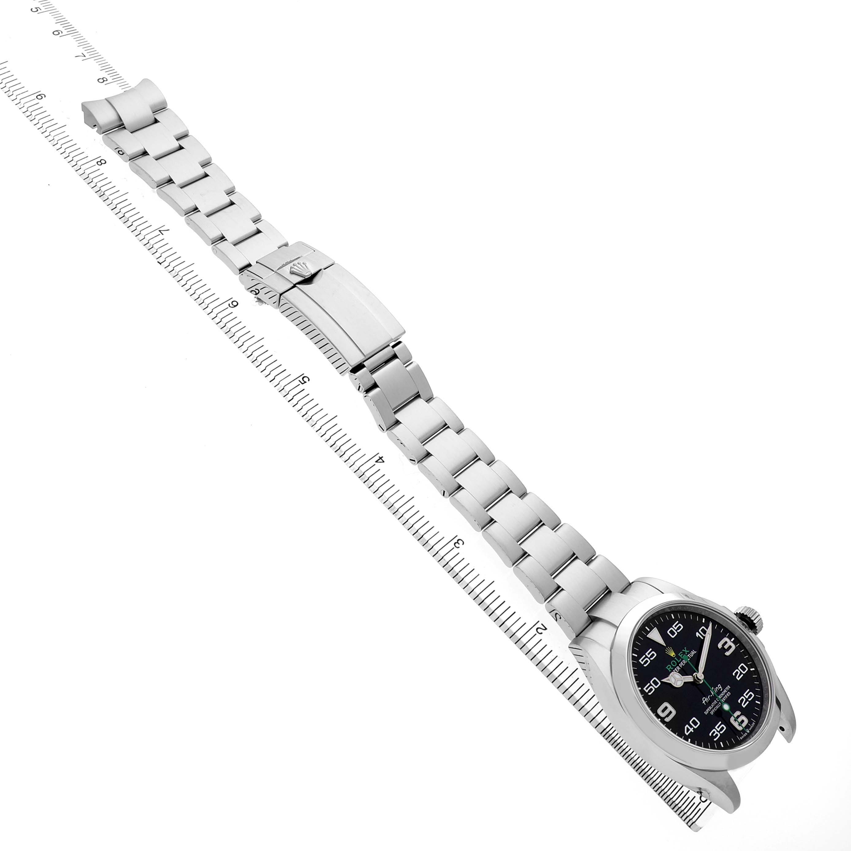 The image shows a top view of a Rolex Air-King M126900-0001 Men's Stainless Steel Black Dial watch, highlighting the bracelet, clasp, and face placed beside a ruler.