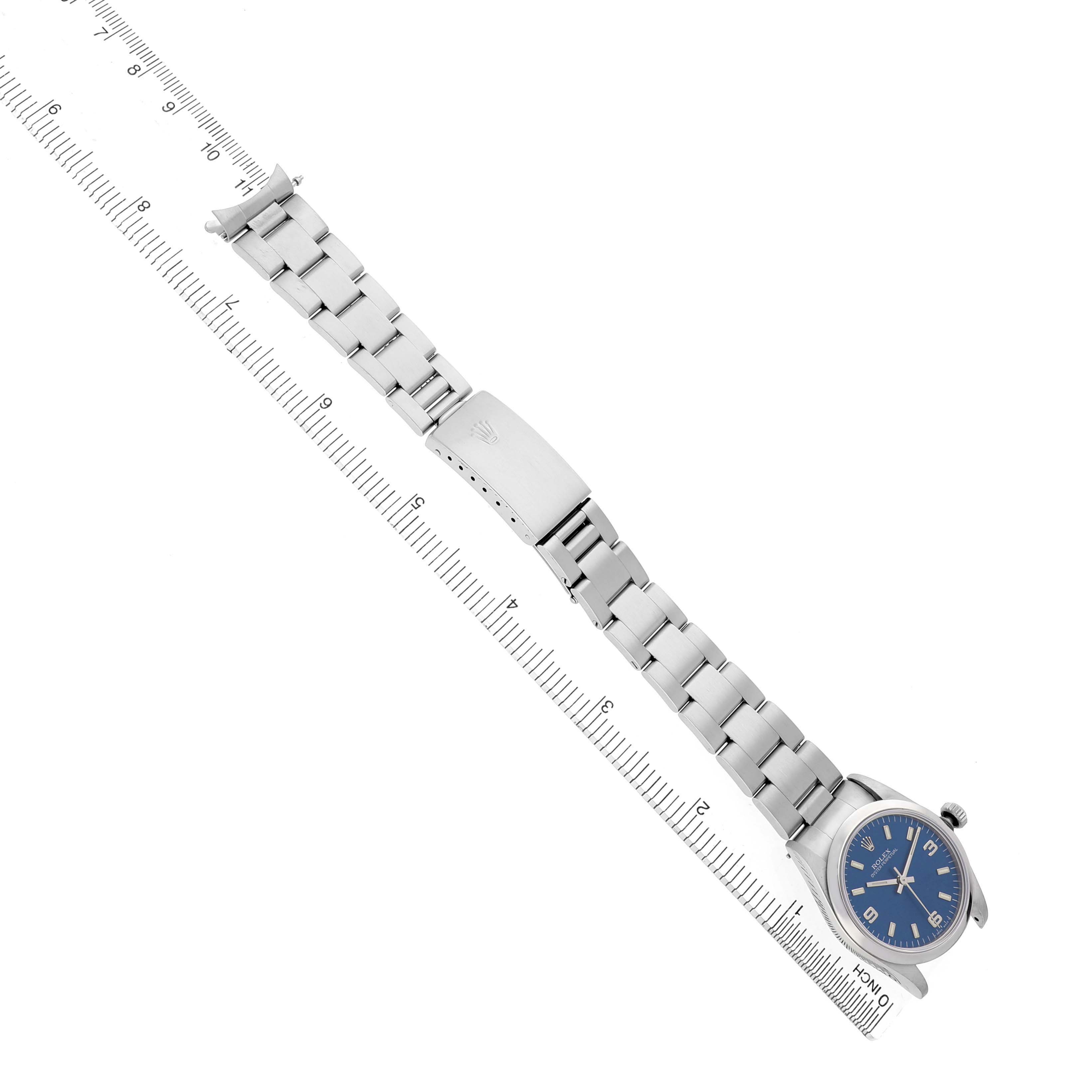The Rolex Mid-Size 67480 Women's Stainless Steel Blue Dial watch is shown from an overhead view, displaying the bracelet, clasp, and watch face alongside a ruler for scale.