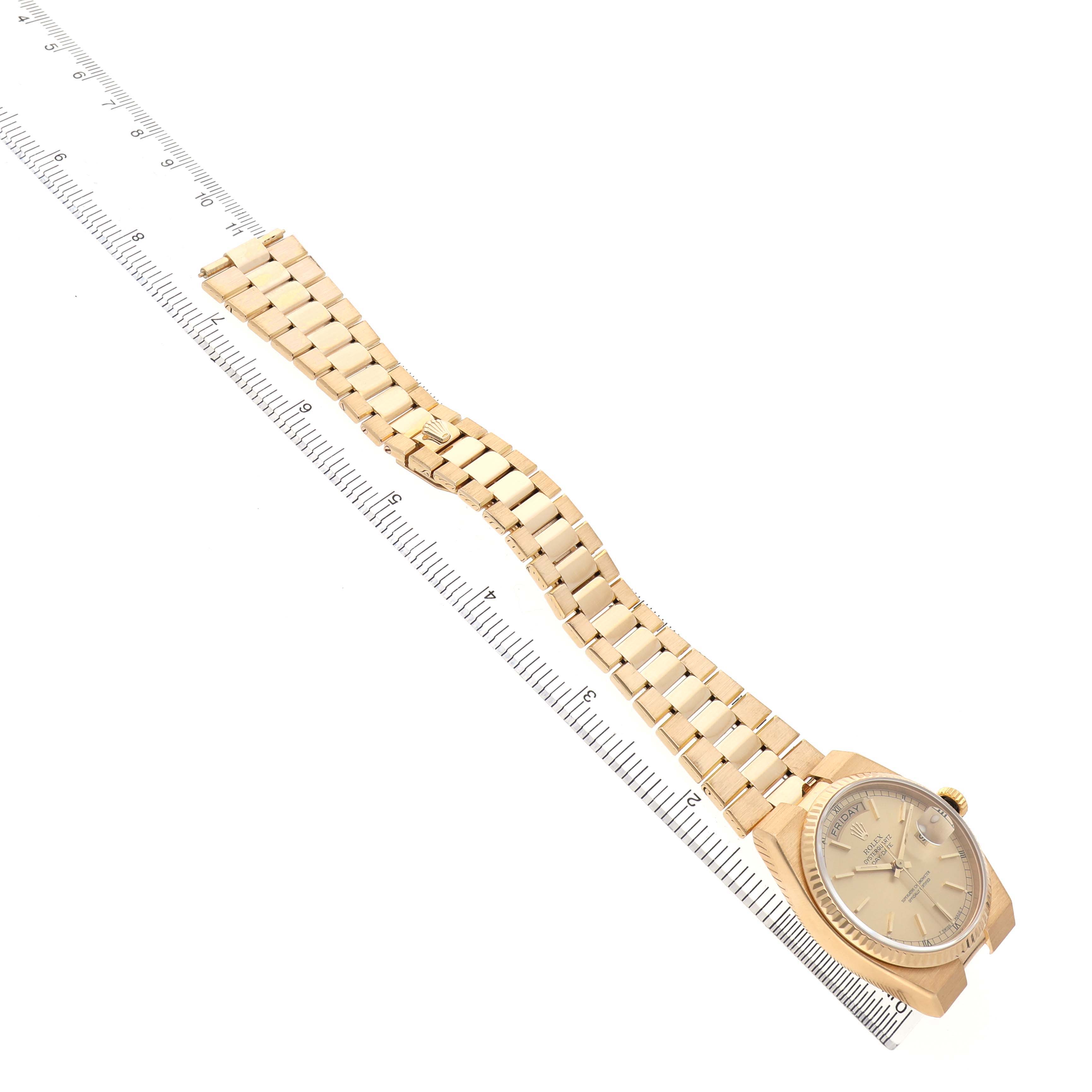 The Rolex President 82028 Men's Yellow Gold Champagne Dial watch is shown at a diagonal angle, displaying the face, bracelet, and clasp alongside a ruler for scale.