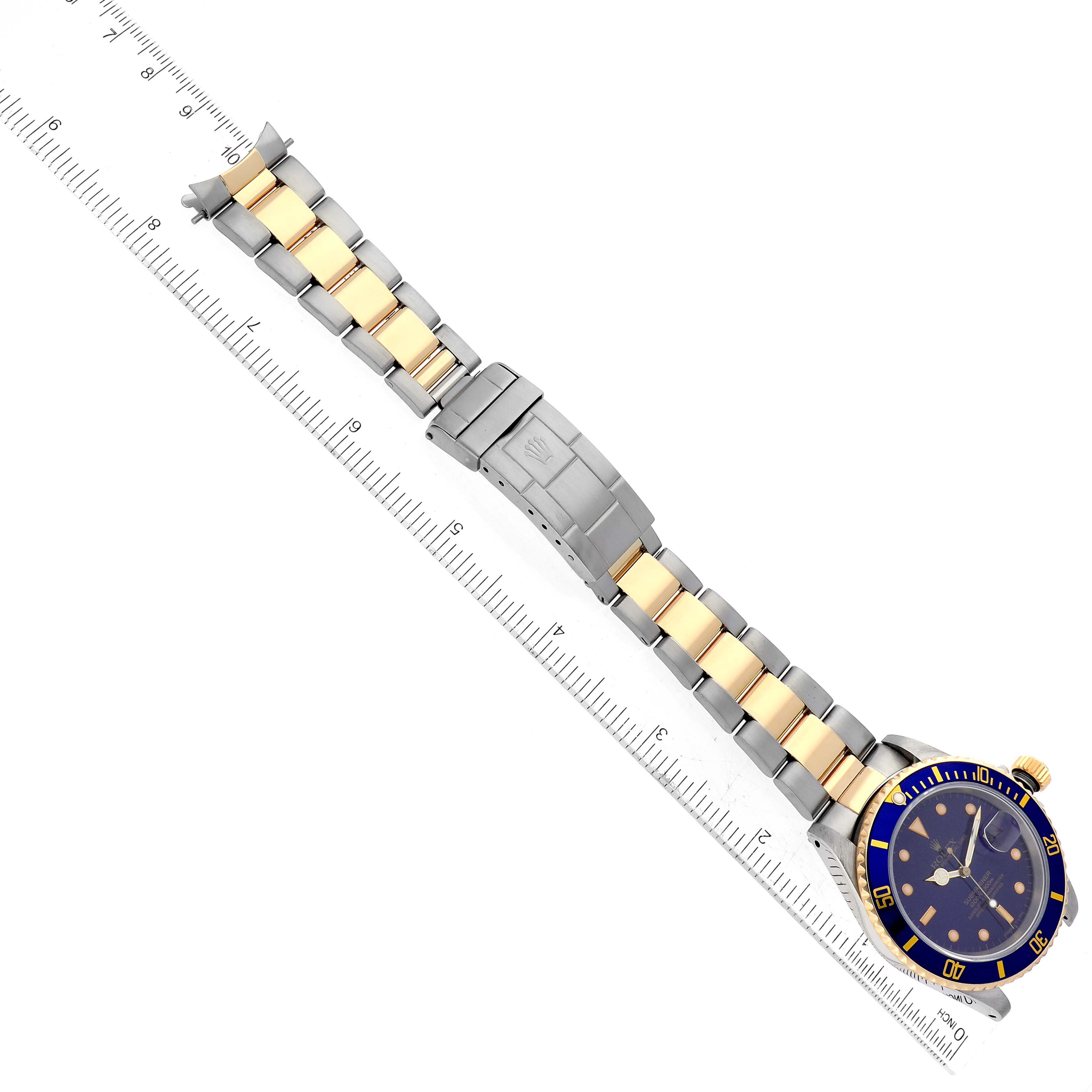 This Rolex Submariner 16613 Men's Steel and Gold (two tone) Blue Dial 16613 Men's Steel and Gold (two tone) Blue Dial watch is shown from a top-down angle, displaying the face, bezel, band, and clasp next to a ruler.