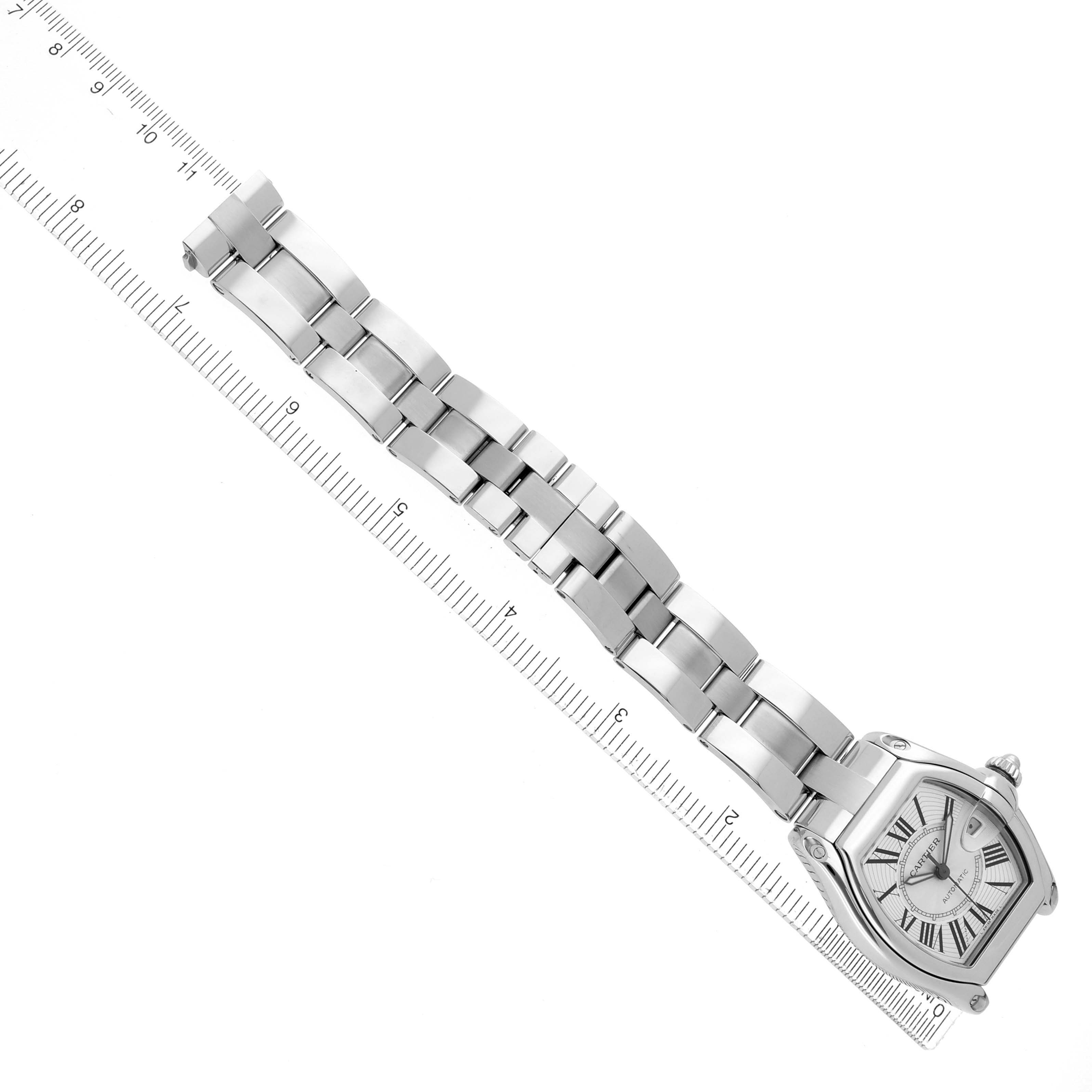 The image shows the Cartier Roadster model W62025V3 men
s watch at a top angle, displaying the watch face, case, and full metal bracelet alongside a ruler.