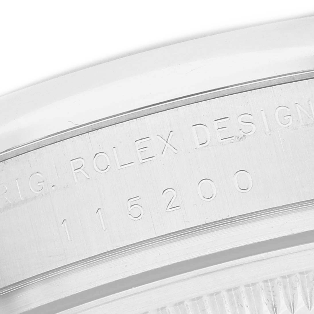 This image shows a close-up of the engraved serial number and "Rolex Design" text on the casing of a Rolex Date 115200 Men
s Stainless Steel Black Dial 115200 Men
s Stainless Steel Black Dial model watch.