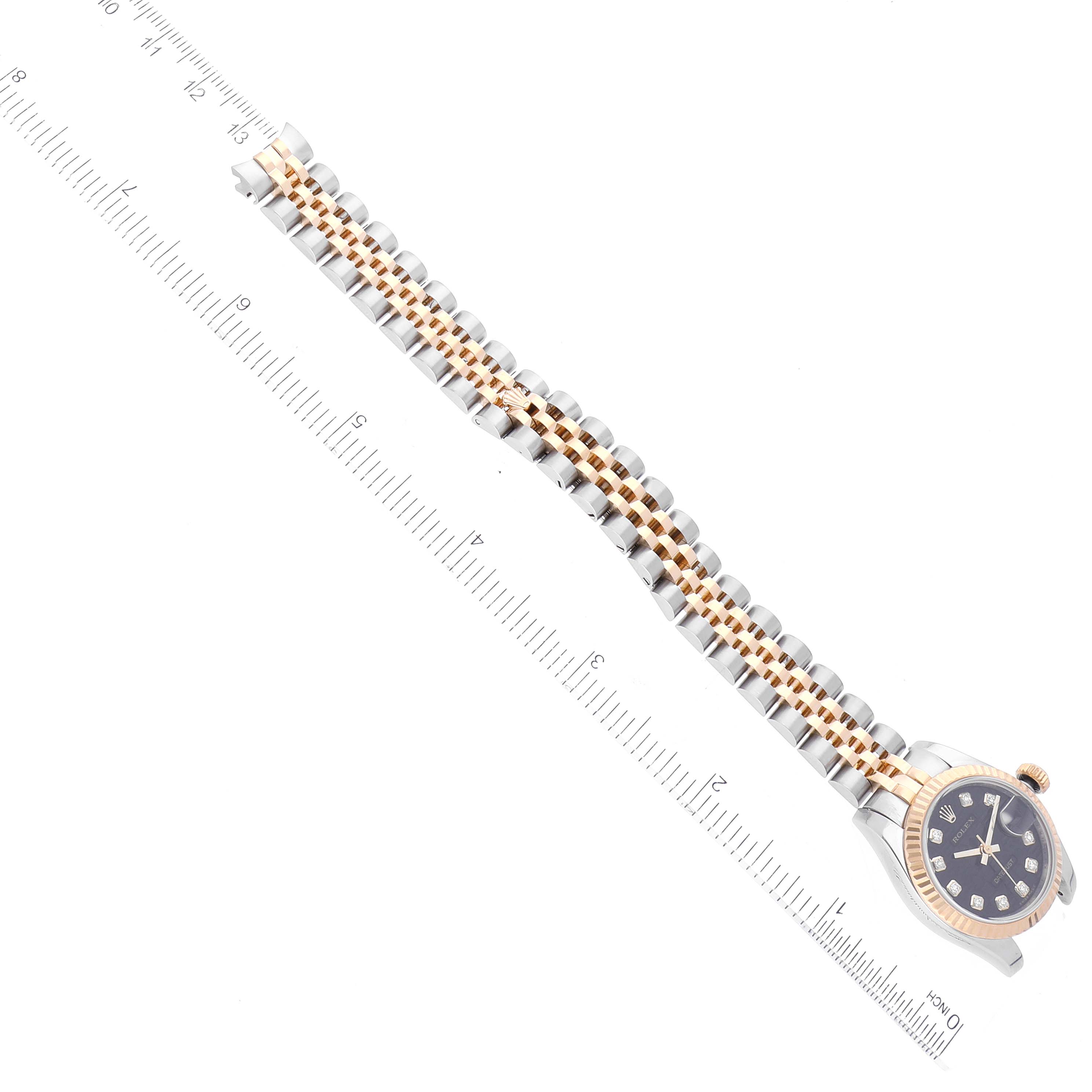 The image shows a Rolex Datejust 179173 Women's Steel and Gold (two tone) Black Dial 179173 Women's Steel and Gold (two tone) Black Dial watch with its bracelet and dial aligned next to a ruler, viewed from above.