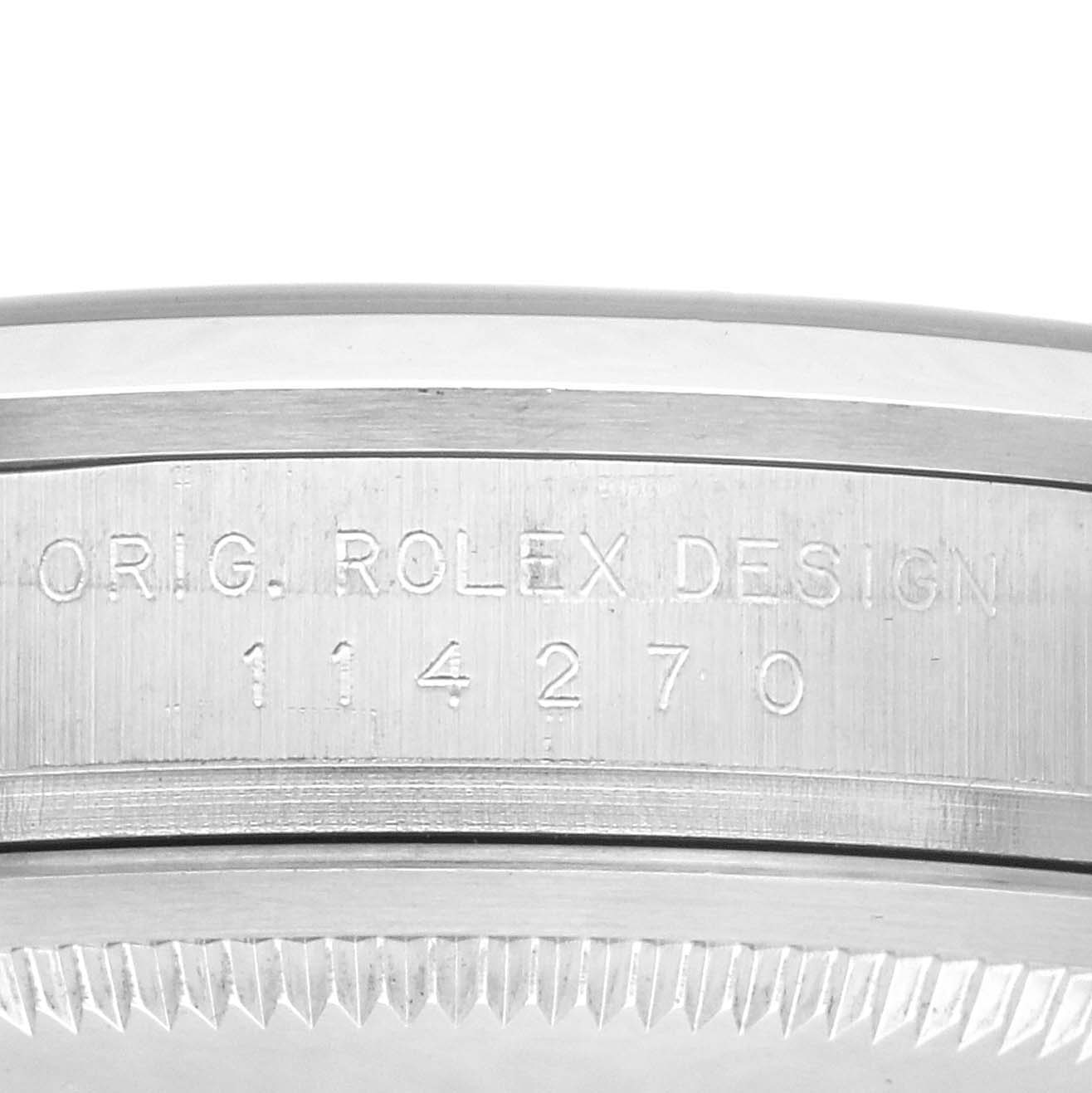 The image shows a close-up of the engraved side of a Rolex Explorer, model number 114270, displaying "ORIG. ROLEX DESIGN" with its brushed metal surface and ridged edge.