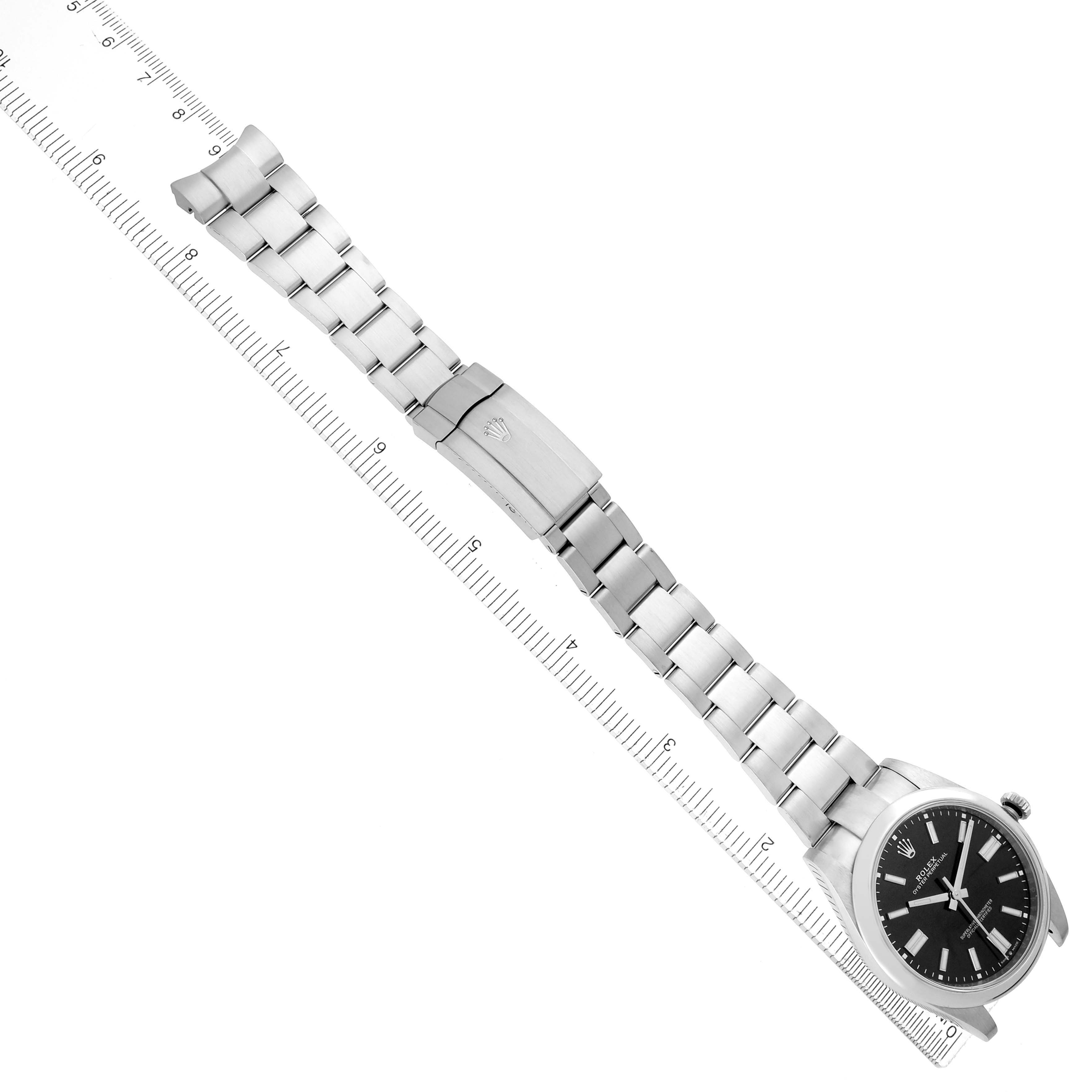 The image shows a Rolex Oyster Perpetual model 124300 men
s watch at a diagonal angle, displaying the full bracelet and clasp alongside a ruler.