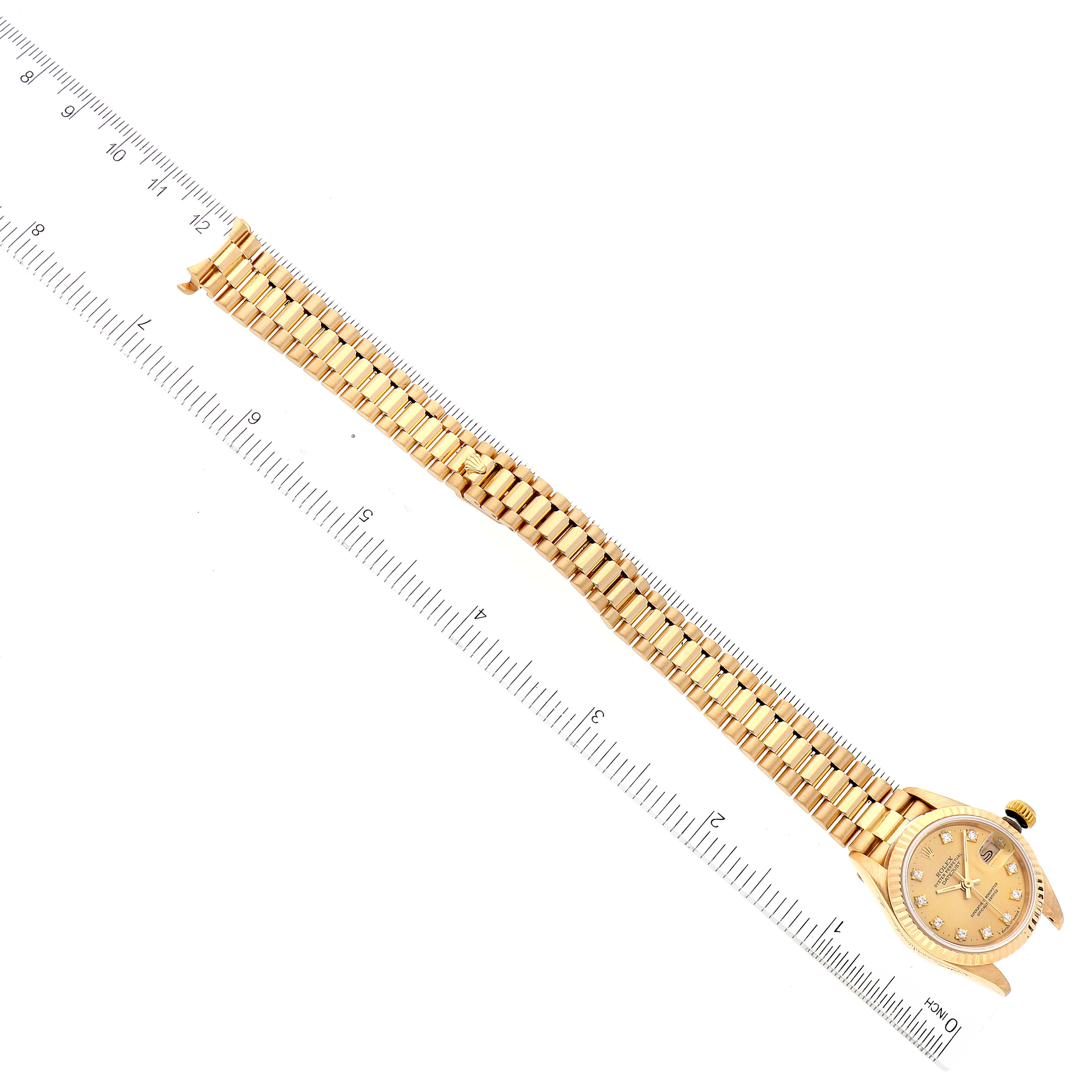 The image shows a Rolex President 69178 Women
s Yellow Gold Champagne Dial 69178 Women
s Yellow Gold Champagne Dial model watch lying flat with its face and full bracelet visible, alongside a ruler for scale.