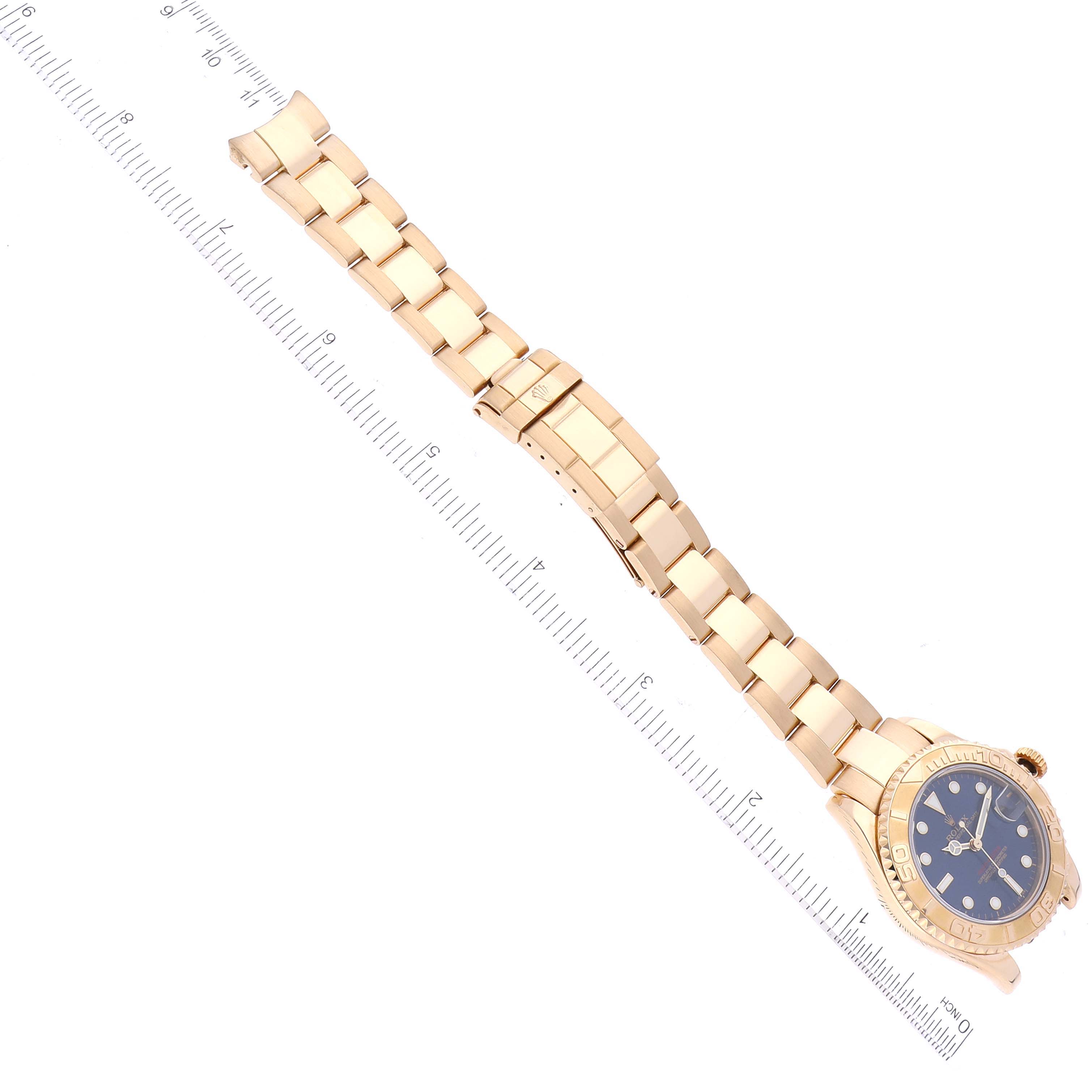 The Rolex Yacht-Master 68628 Men's Yellow Gold Blue Dial 68628 Men's Yellow Gold Blue Dial watch is shown from a top view, displaying its gold bracelet, blue dial, and the measurement ruler beside it.