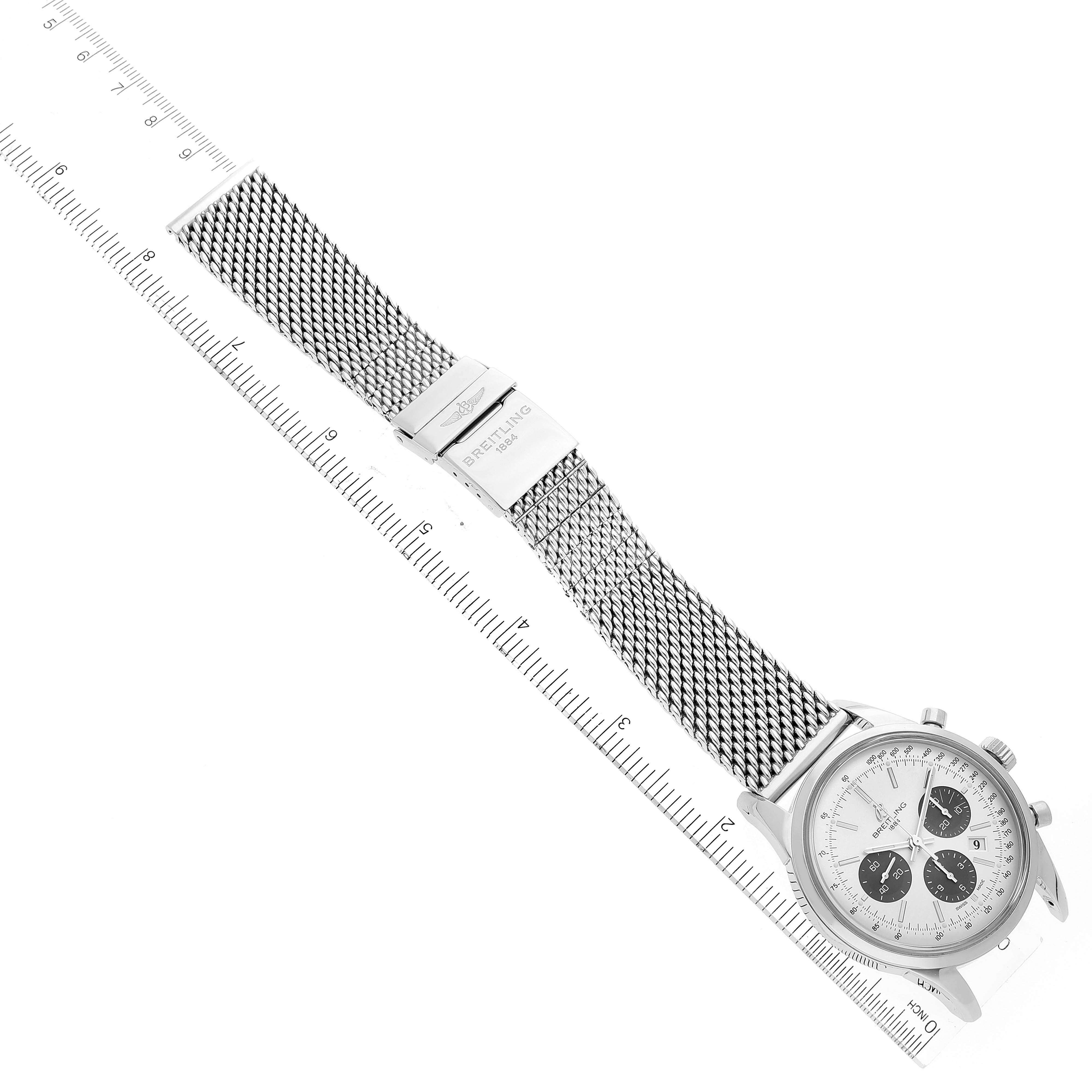 The image shows a Breitling Transocean AB015212/G724 Men's Stainless Steel Silver Dial AB015212/G724 Men's Stainless Steel Silver Dial watch at an angle with its face, mesh band, and clasp, laid alongside a ruler.