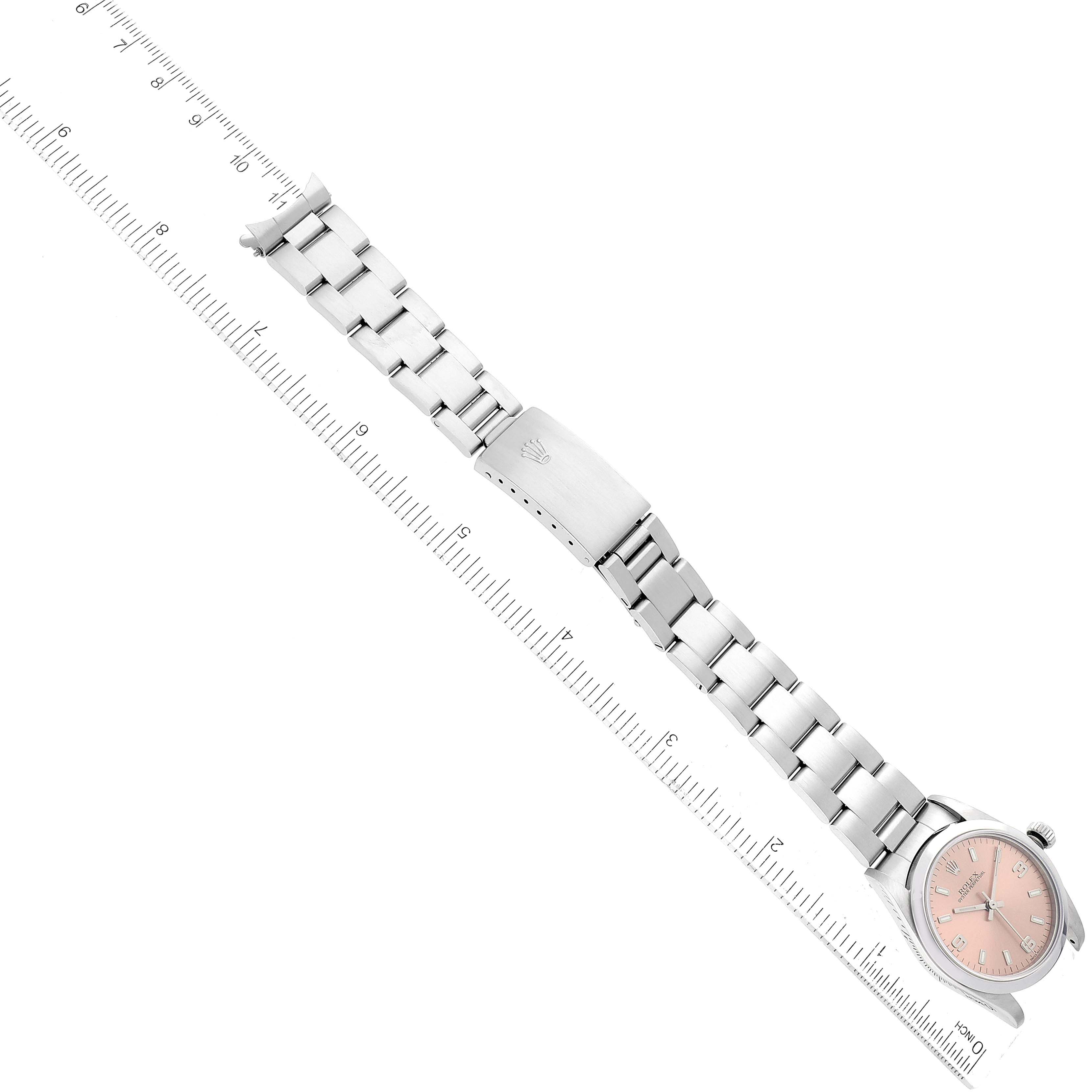 The image shows a Rolex Mid-Size 77080 Women's Stainless Steel Pink Dial 77080 Women's Stainless Steel Pink Dial model watch from a top-down angle, displaying its entire band, clasp, and face beside a ruler.