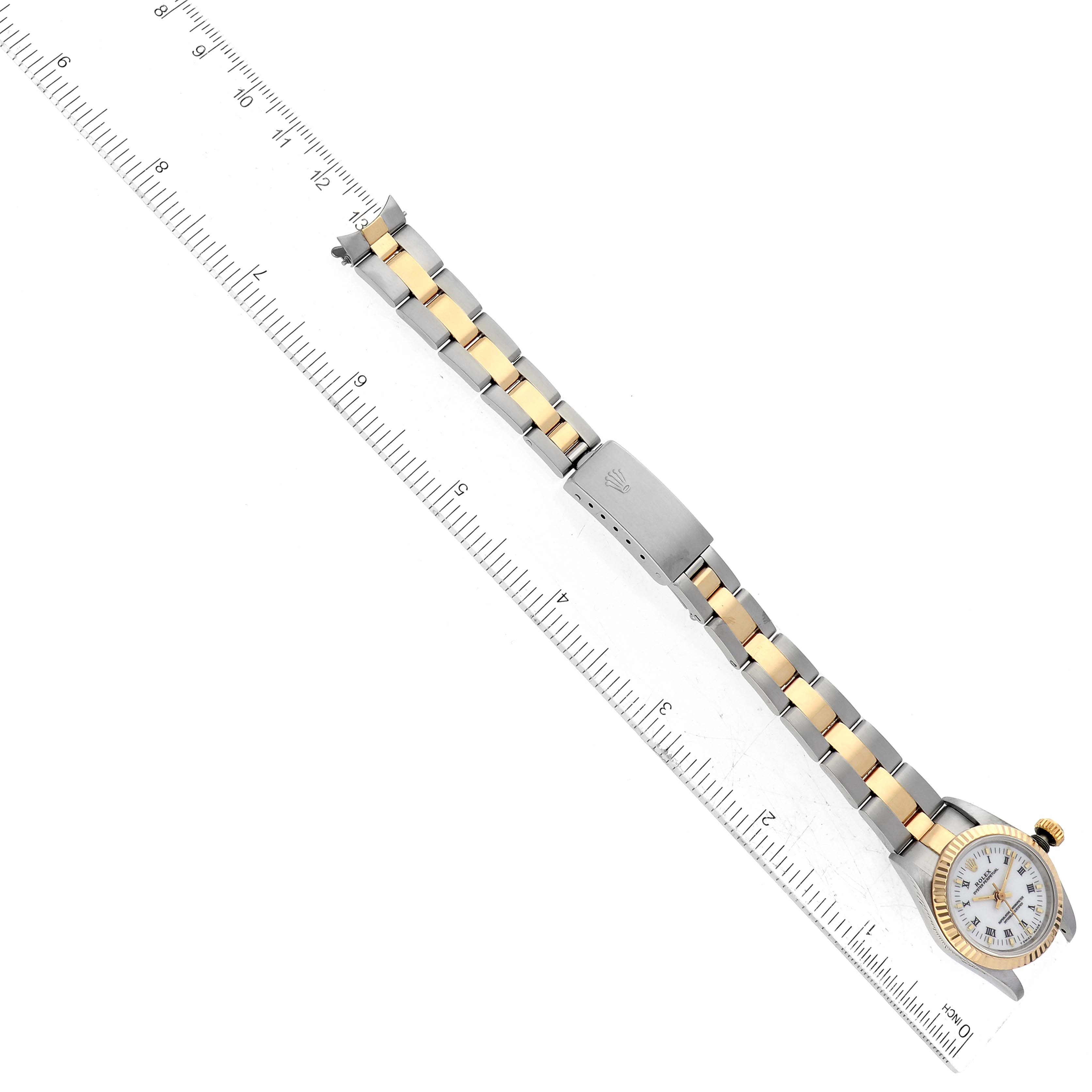 The image shows a top view of a Rolex Oyster Perpetual 67193 Women
s Steel and Gold (two tone) White Dial 67193 Women
s Steel and Gold (two tone) White Dial watch, highlighting the face, two-tone bracelet, and clasp, placed next to a ruler.