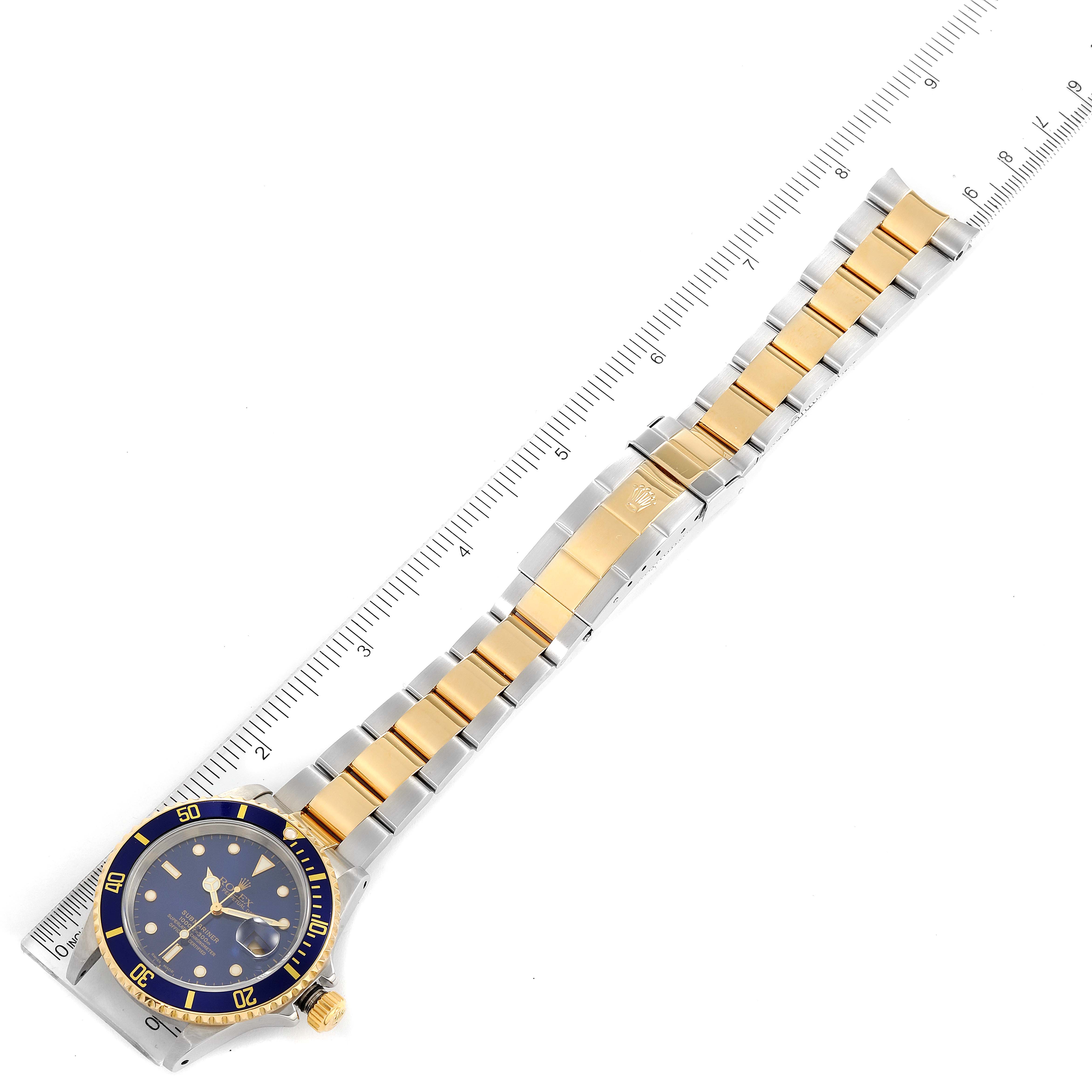 The image shows a Rolex Submariner 16613 Men
s Steel and Gold (two tone) Blue Dial 16613 Men
s Steel and Gold (two tone) Blue Dial watch featuring the front face and full bracelet placed next to a ruler for measurement.