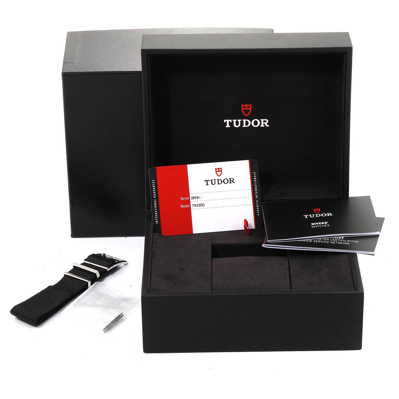 The image shows the packaging contents of a Tudor Heritage Black Bay 79230G Men
s Stainless Steel Black Dial 79230G Men
s Stainless Steel Black Dial watch, including the box, warranty card, and an extra strap.
