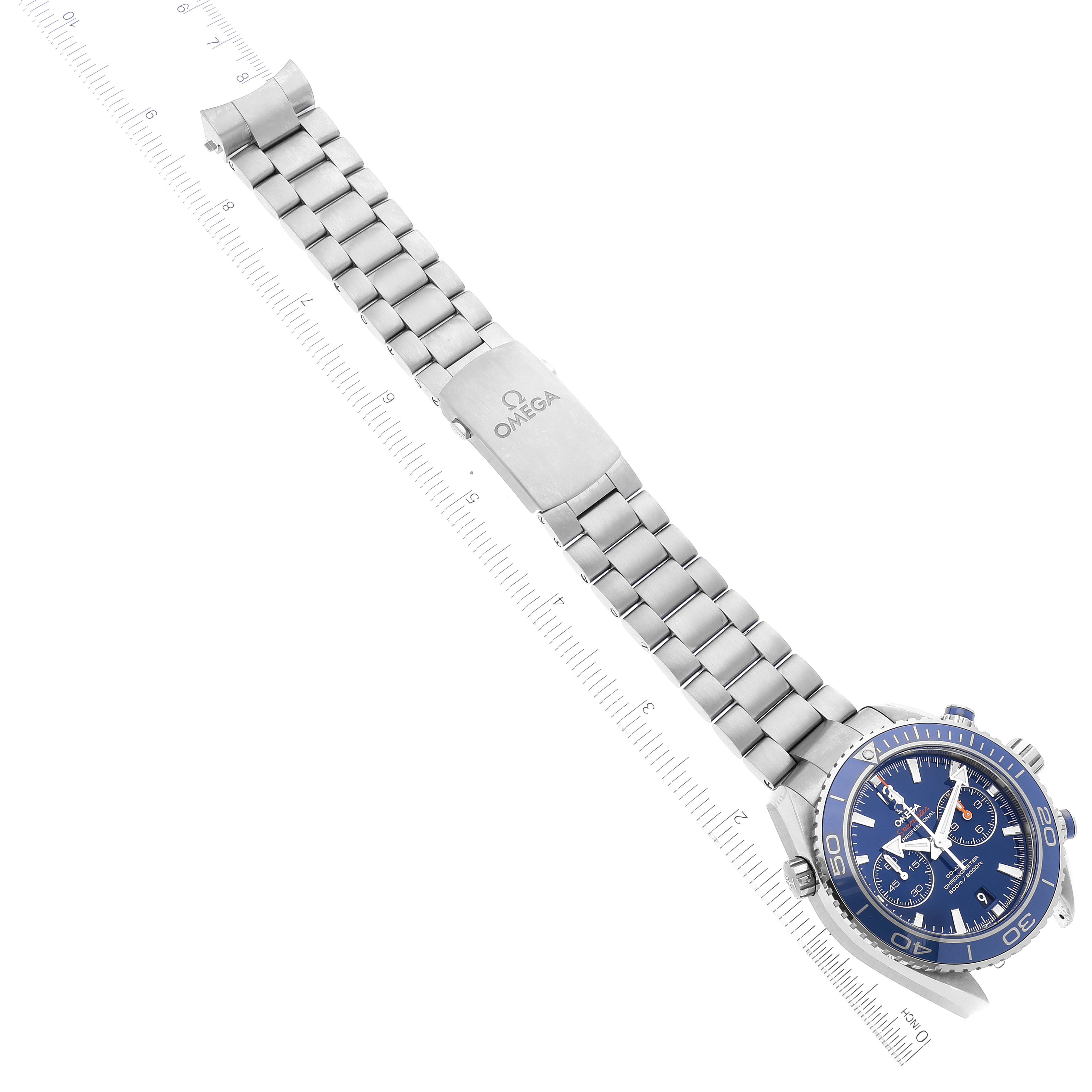 The image shows the Omega Planet Ocean 232.90.46.51.03.001 Men's Stainless Steel Blue Dial 232.90.46.51.03.001 Men's Stainless Steel Blue Dial watch with a full view of the bracelet and clasp, laid out diagonally alongside a ruler.