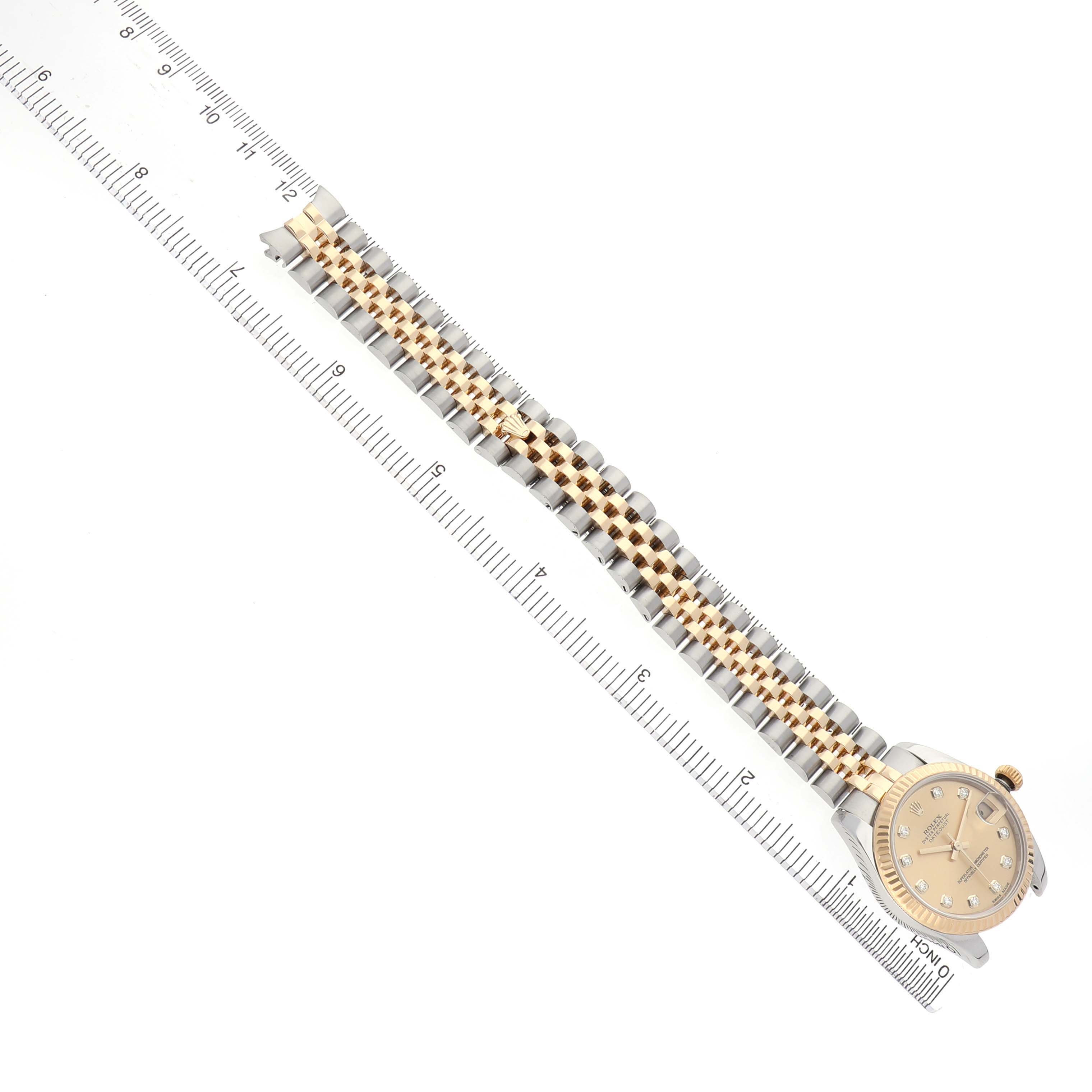 The Rolex Mid-Size 178273 Women's Steel and Gold (two tone) Champagne Dial watch is shown from a top view, displaying the face and full bracelet alongside a ruler.