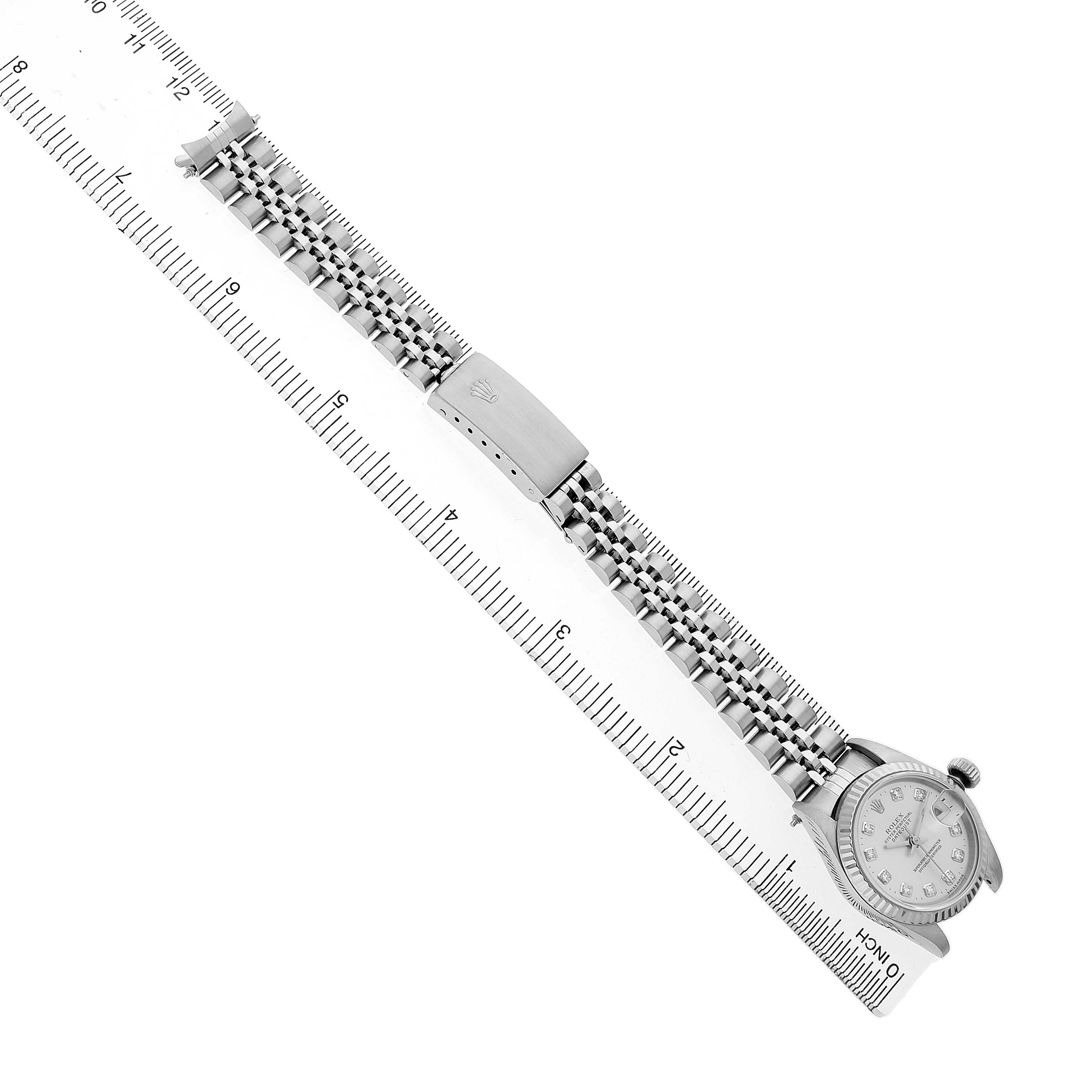 The Rolex Datejust 69174 Women's Stainless Steel Silver Dial watch is shown from a top-down angle, highlighting its face, crown, bracelet, and clasp alongside a ruler.