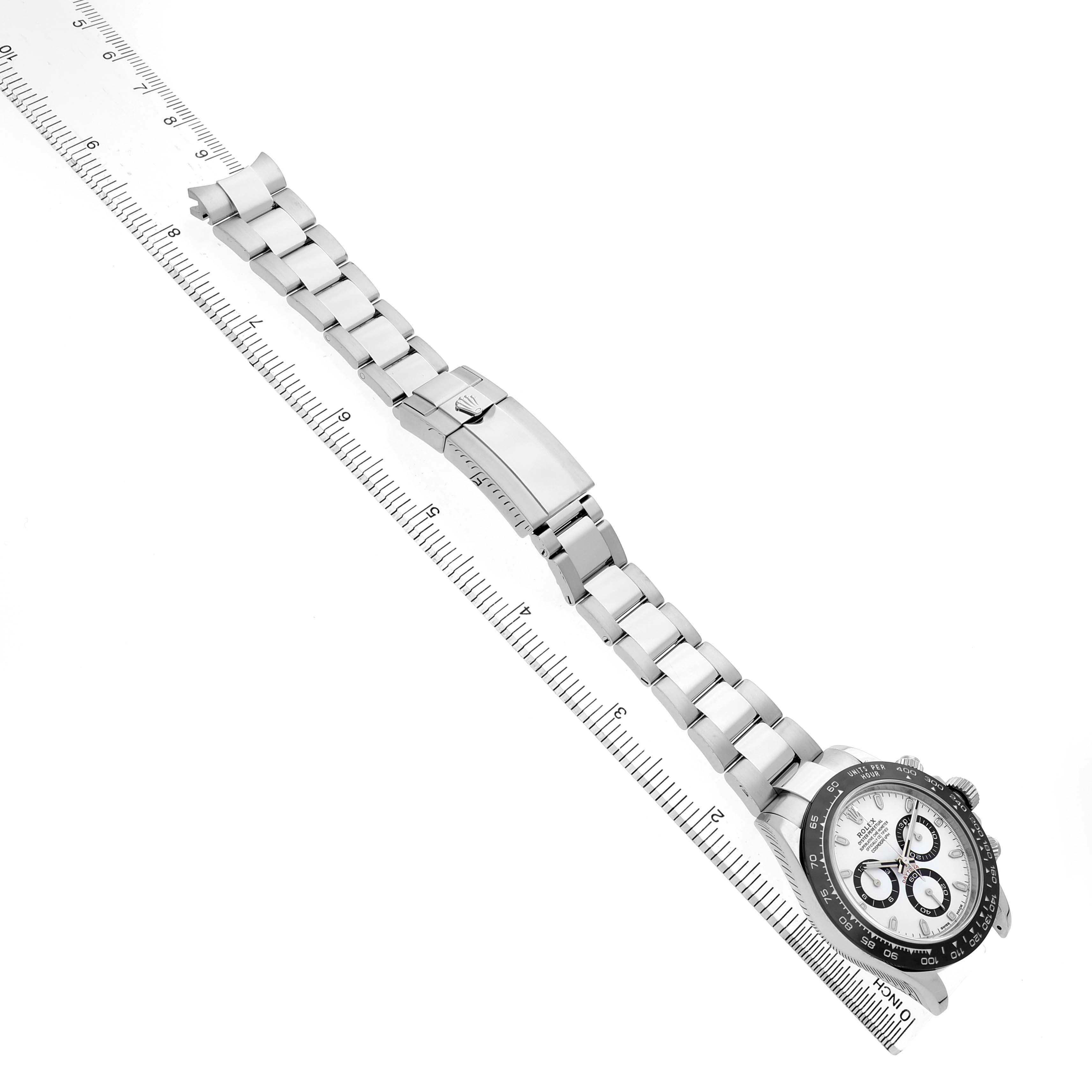 The Rolex Daytona M116500LN-0001 Men's Stainless Steel White Dial watch is shown at a diagonal angle, displaying the bracelet, clasp, and face details alongside a ruler.