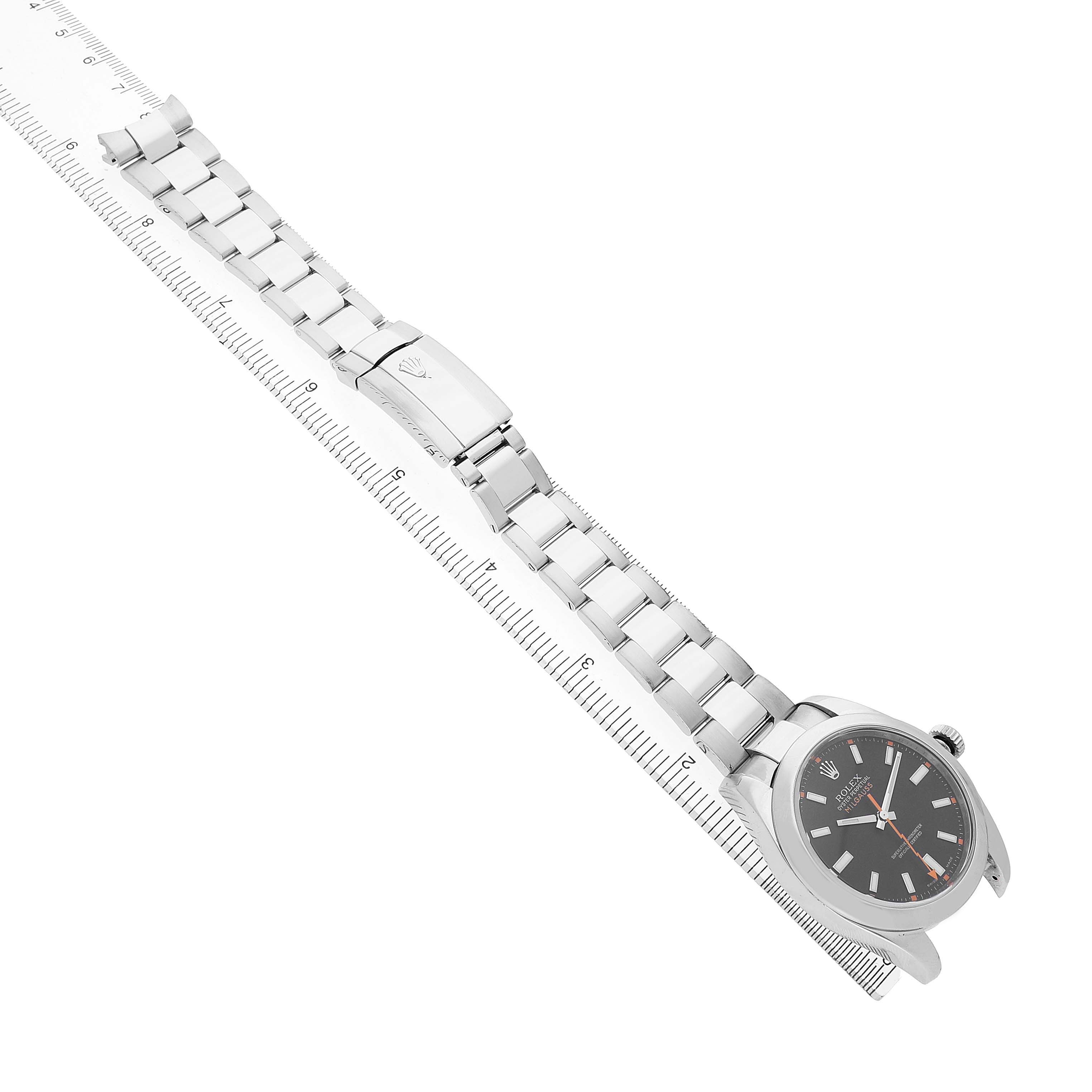 The Rolex Milgauss 116400 Men's Stainless Steel Black Dial watch is shown at a diagonal angle, with the face, bracelet, and clasp visible beside a ruler.