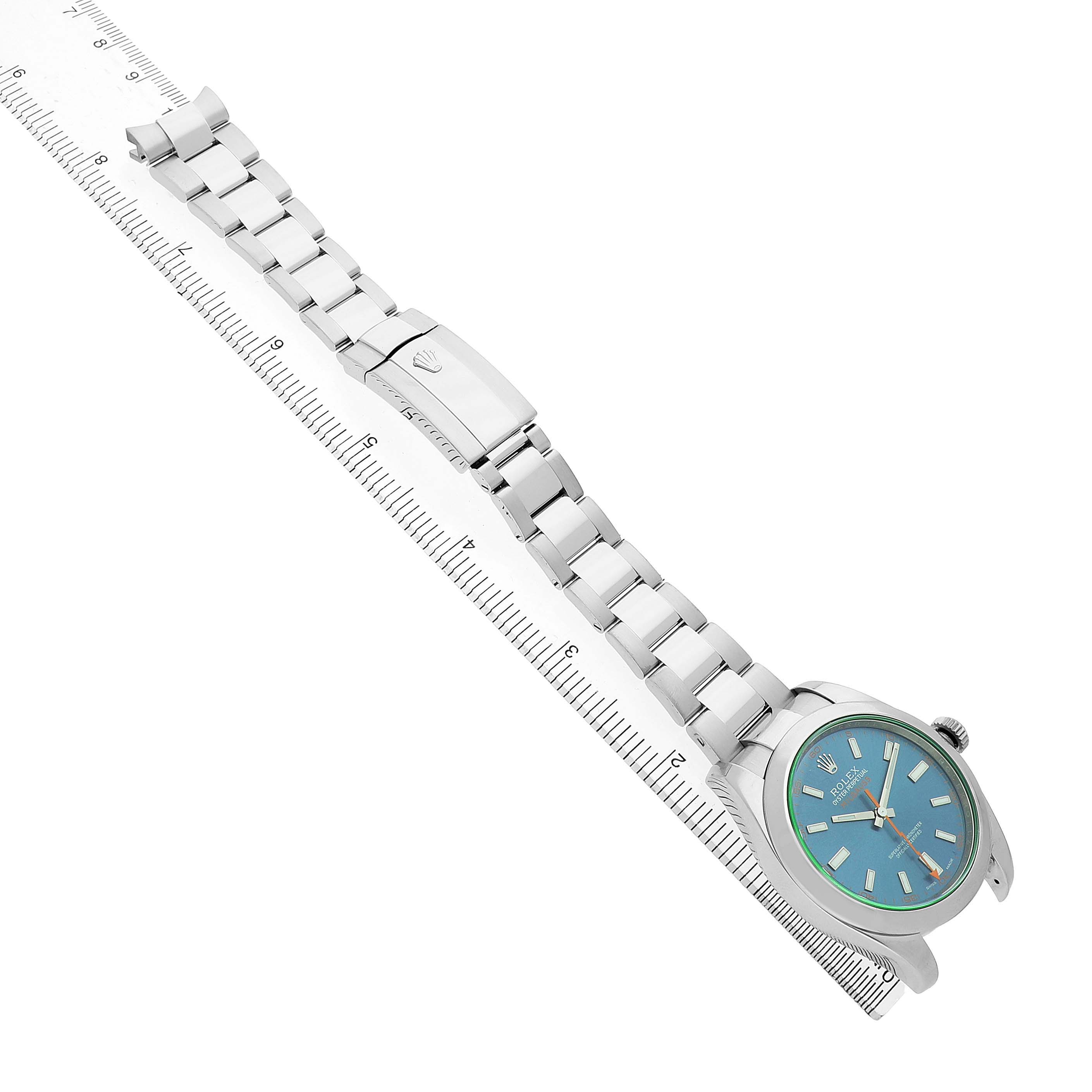 The Rolex Milgauss 116400GV Men's Stainless Steel Blue Dial watch is shown from an angled top view, displaying the face, bracelet, and clasp alongside a ruler.
