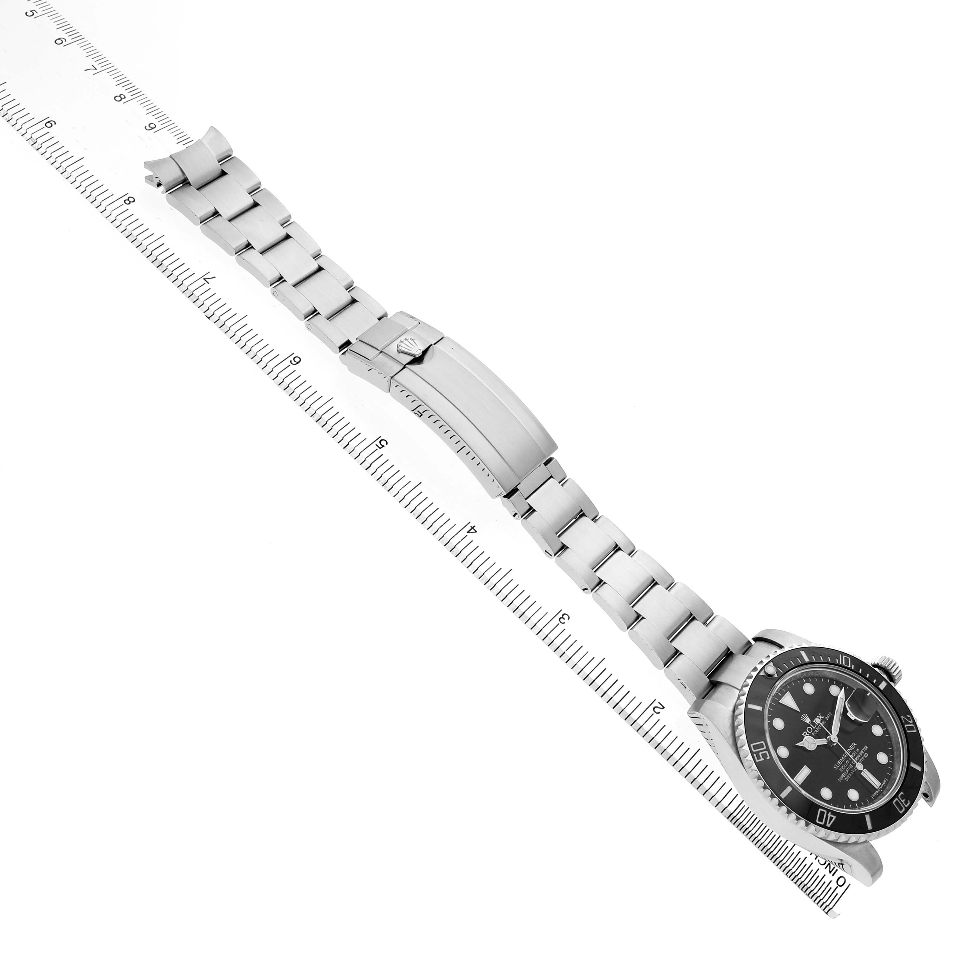 The image shows a Rolex Submariner M116610LN-0001 Men's Stainless Steel Black Dial watch at a top-down angle, displaying its bracelet and clasp fully extended alongside a ruler.