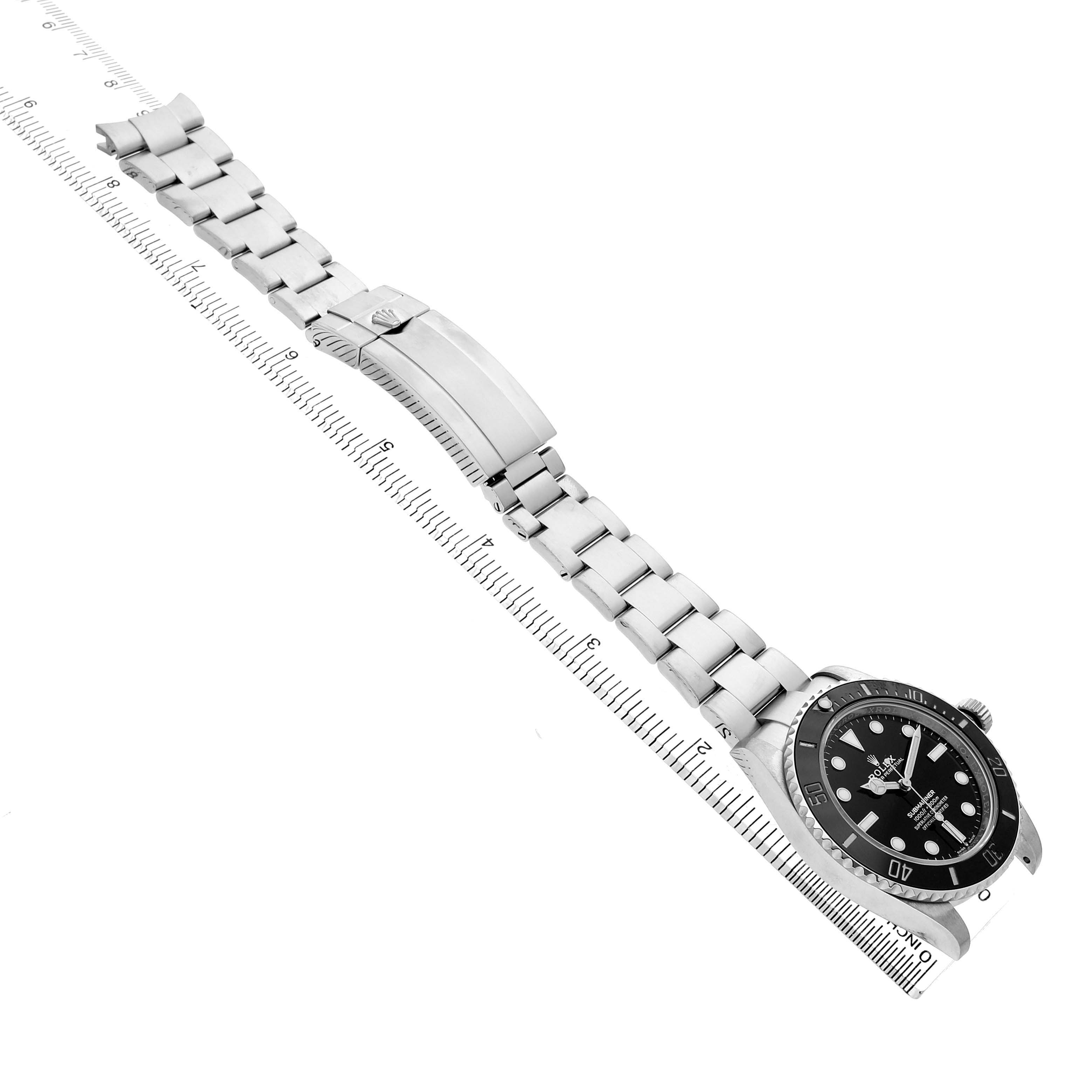 The Rolex Submariner M124060-0001 Men's Stainless Steel Black Dial watch is shown at an angle displaying its bracelet and clasp, aligned along a measuring guide.